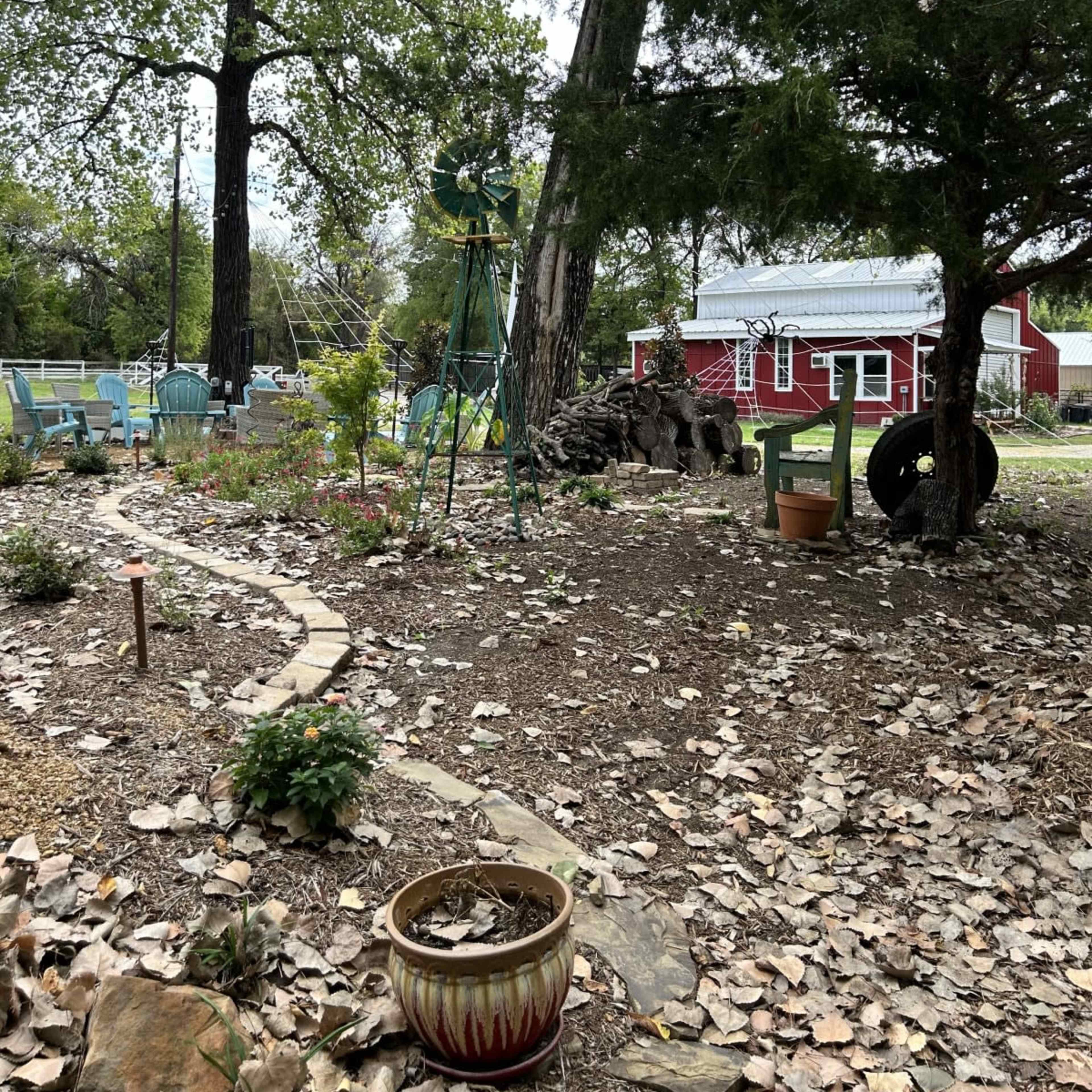 A garden scene features a winding path surrounded by trees, potted plants, and a rustic shed in the background.