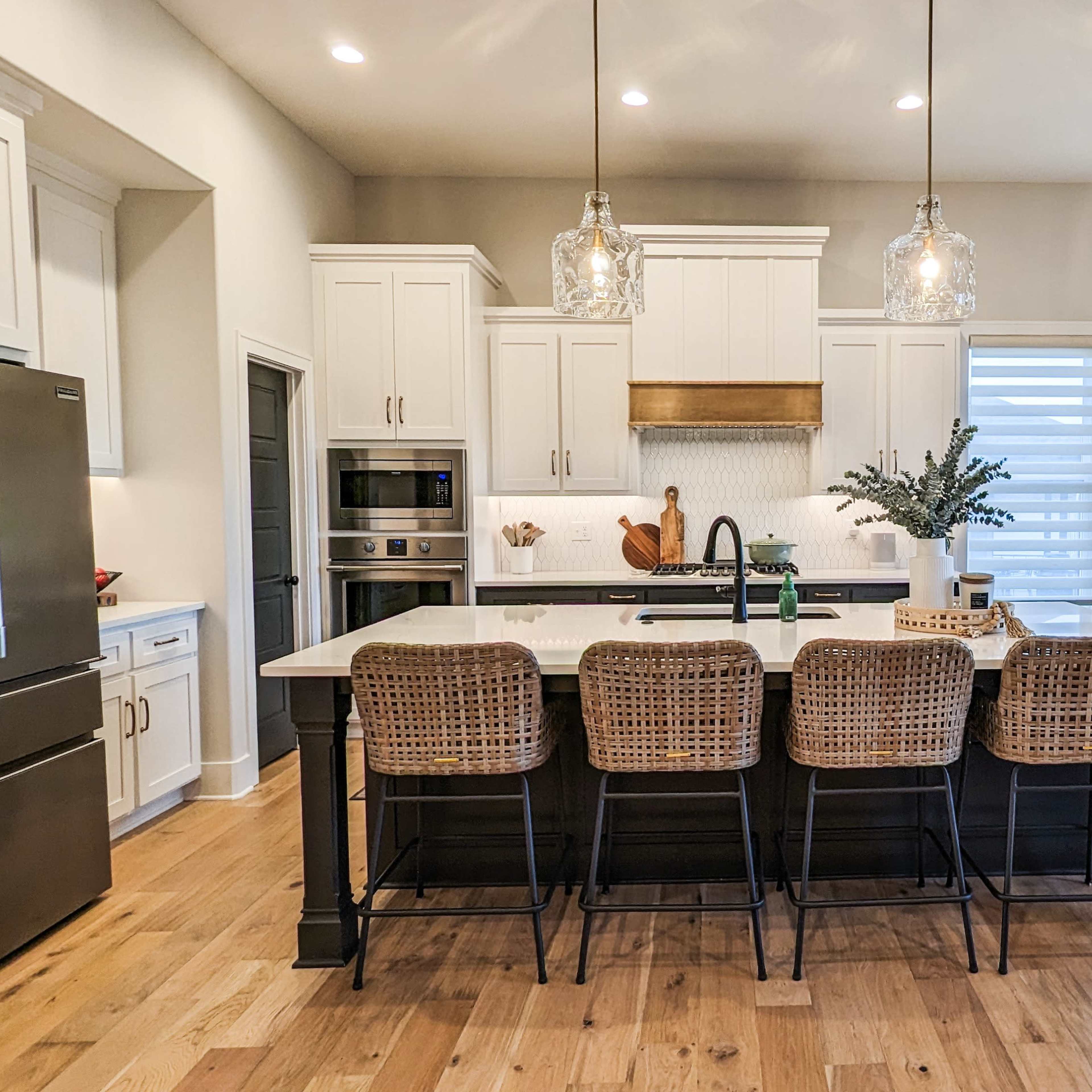 A modern kitchen with white cabinetry, a large island with barstools, and a dining area featuring a table and chairs near large windows.
