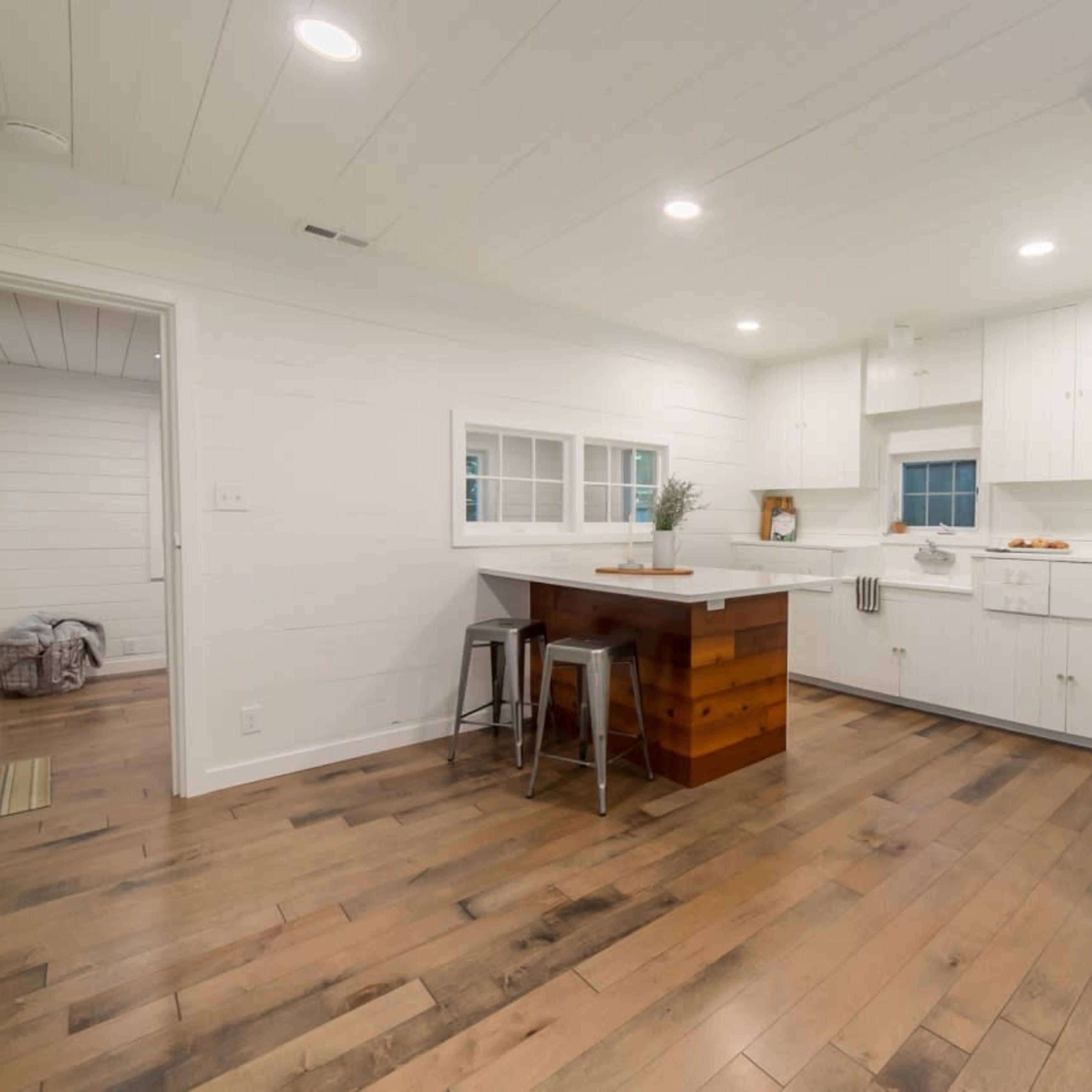 A modern kitchen with white cabinets, a wooden island, and hardwood floors, illuminated by overhead lights.