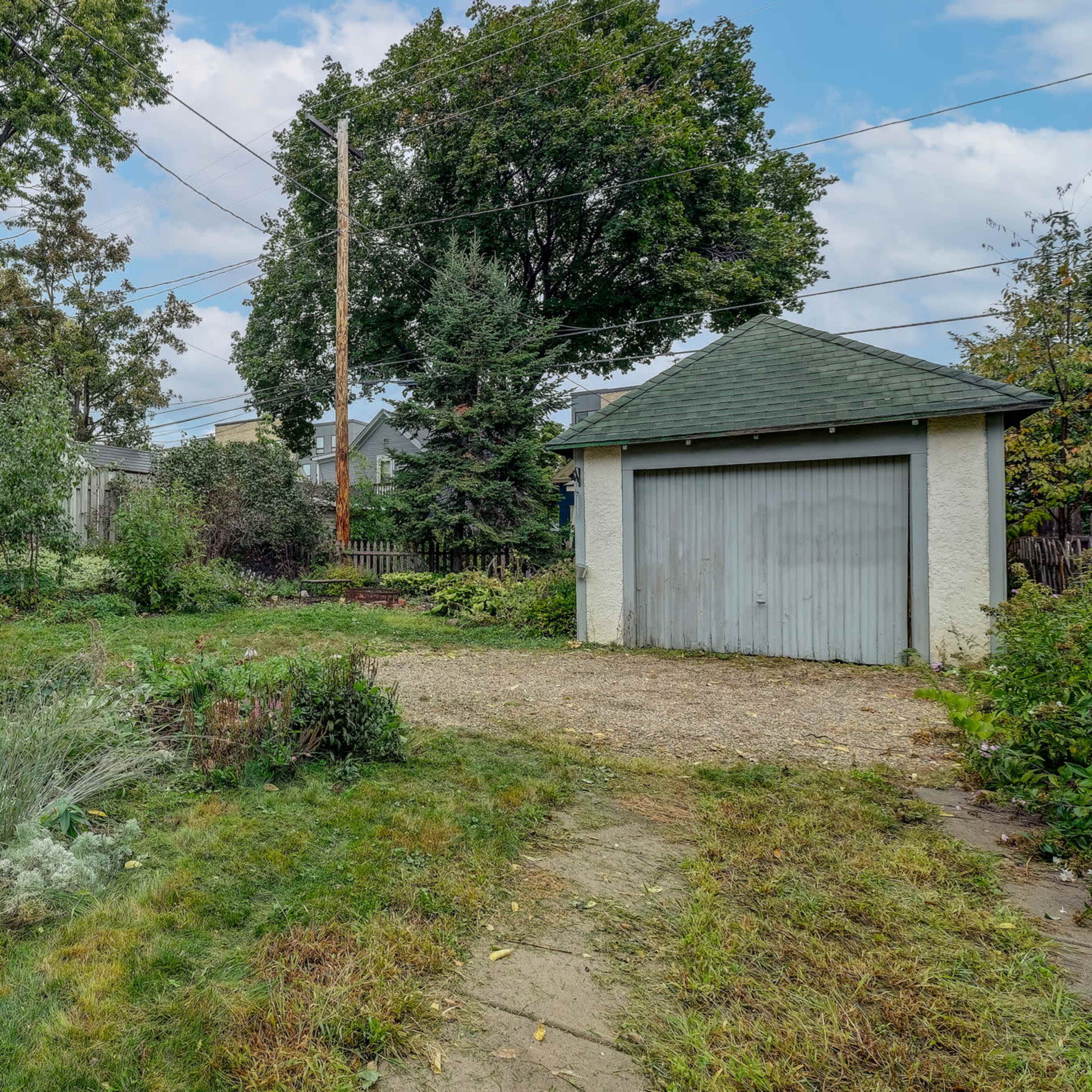 An overgrown backyard with a gravel path leading to a small shed.