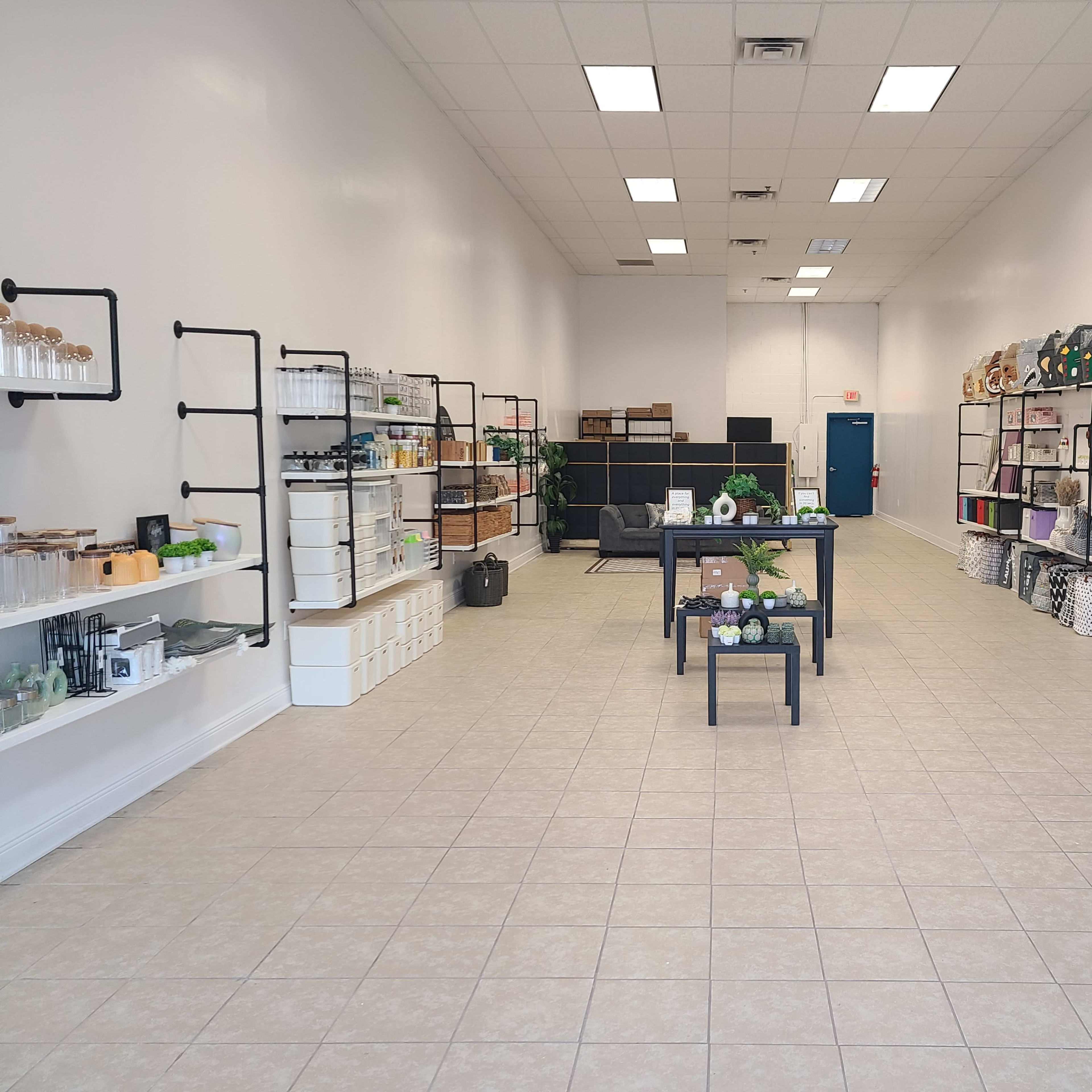 A spacious retail store interior with shelves on both sides displaying various products, and a central display table surrounded by tiled flooring.