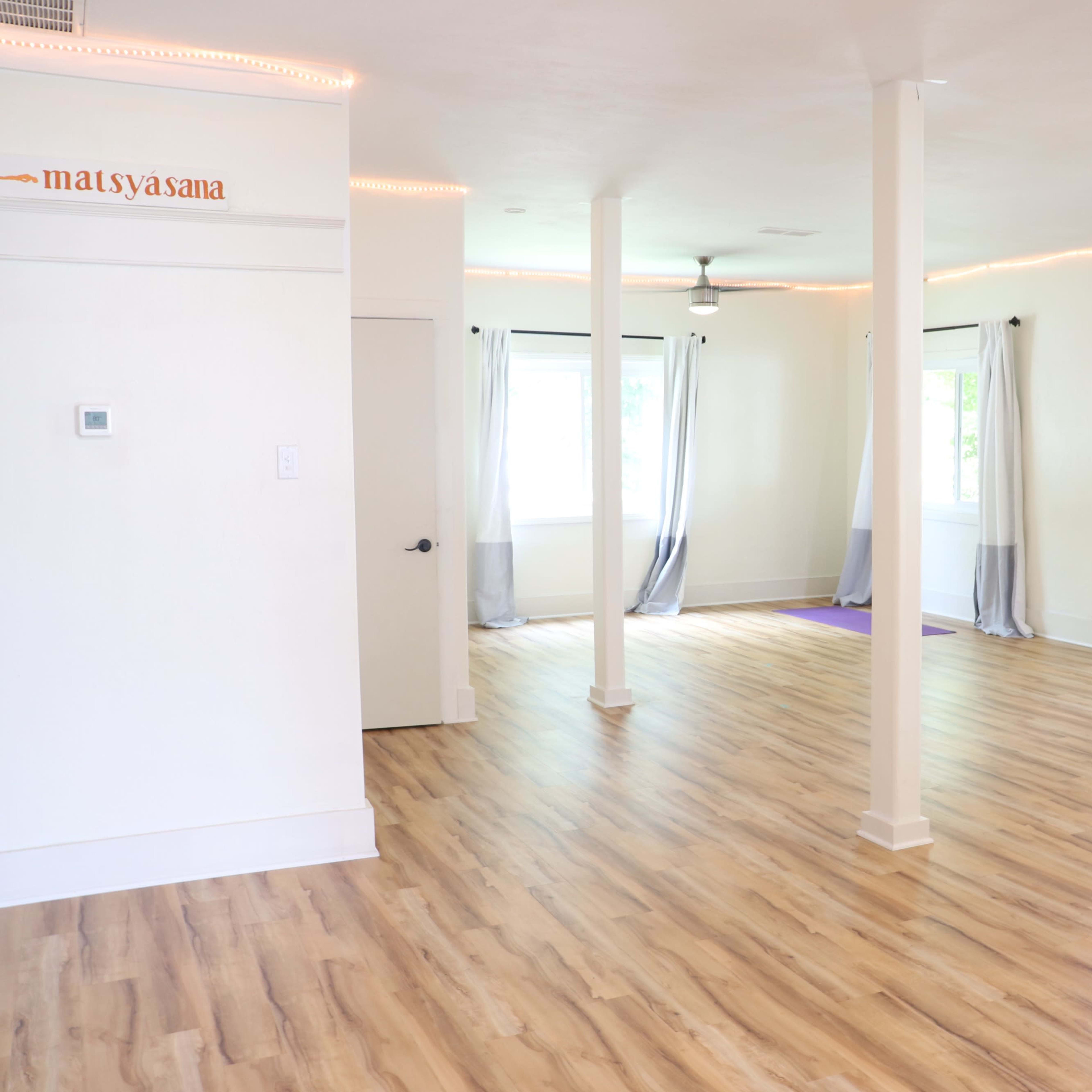 A spacious, well-lit studio with wooden flooring, large windows, and two doors leading outside.