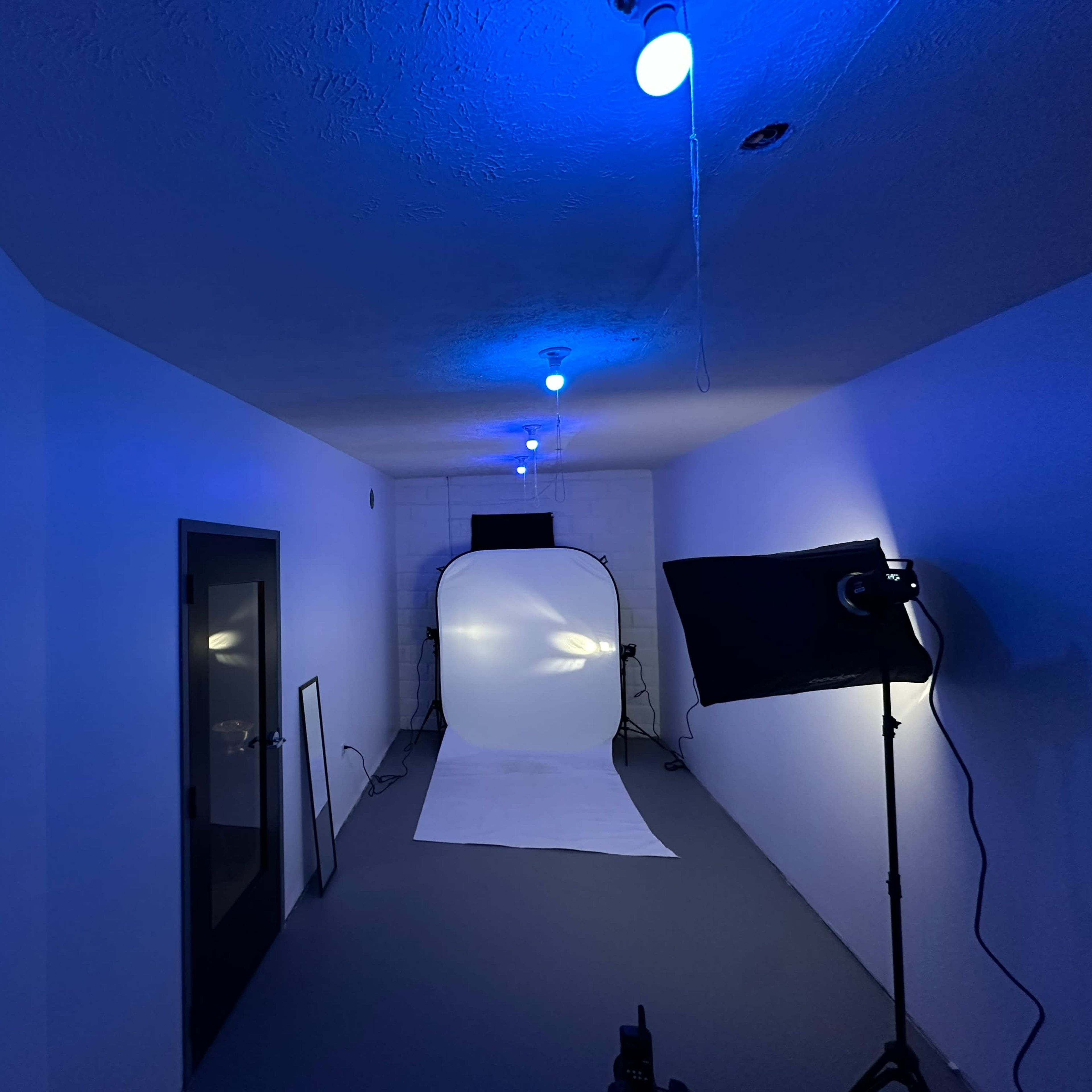 A photography studio with blue lighting, a white backdrop, and a light stand set up in an empty space.