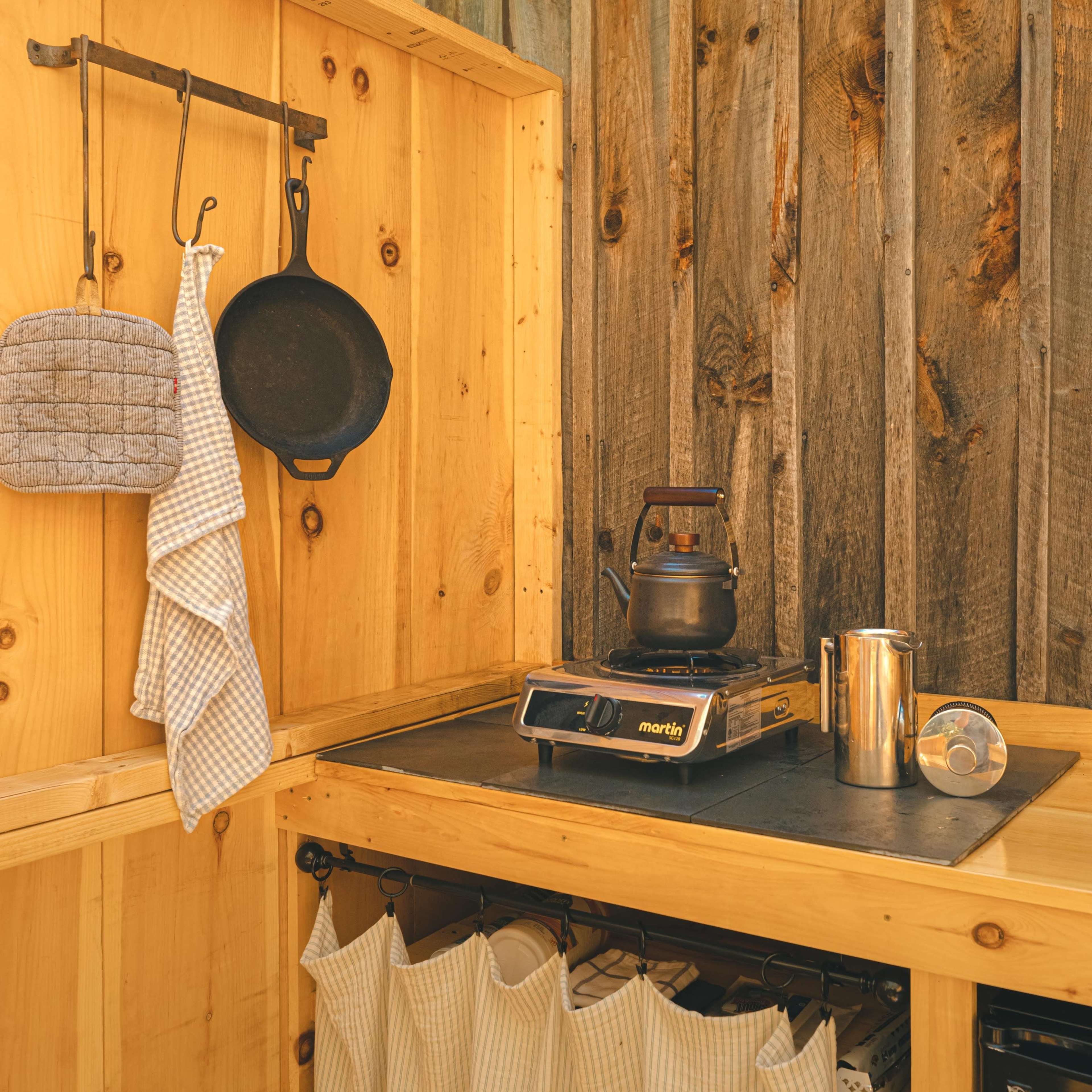 A wooden outdoor kitchen space with a portable stove, hanging cookware, and neatly arranged utensils.