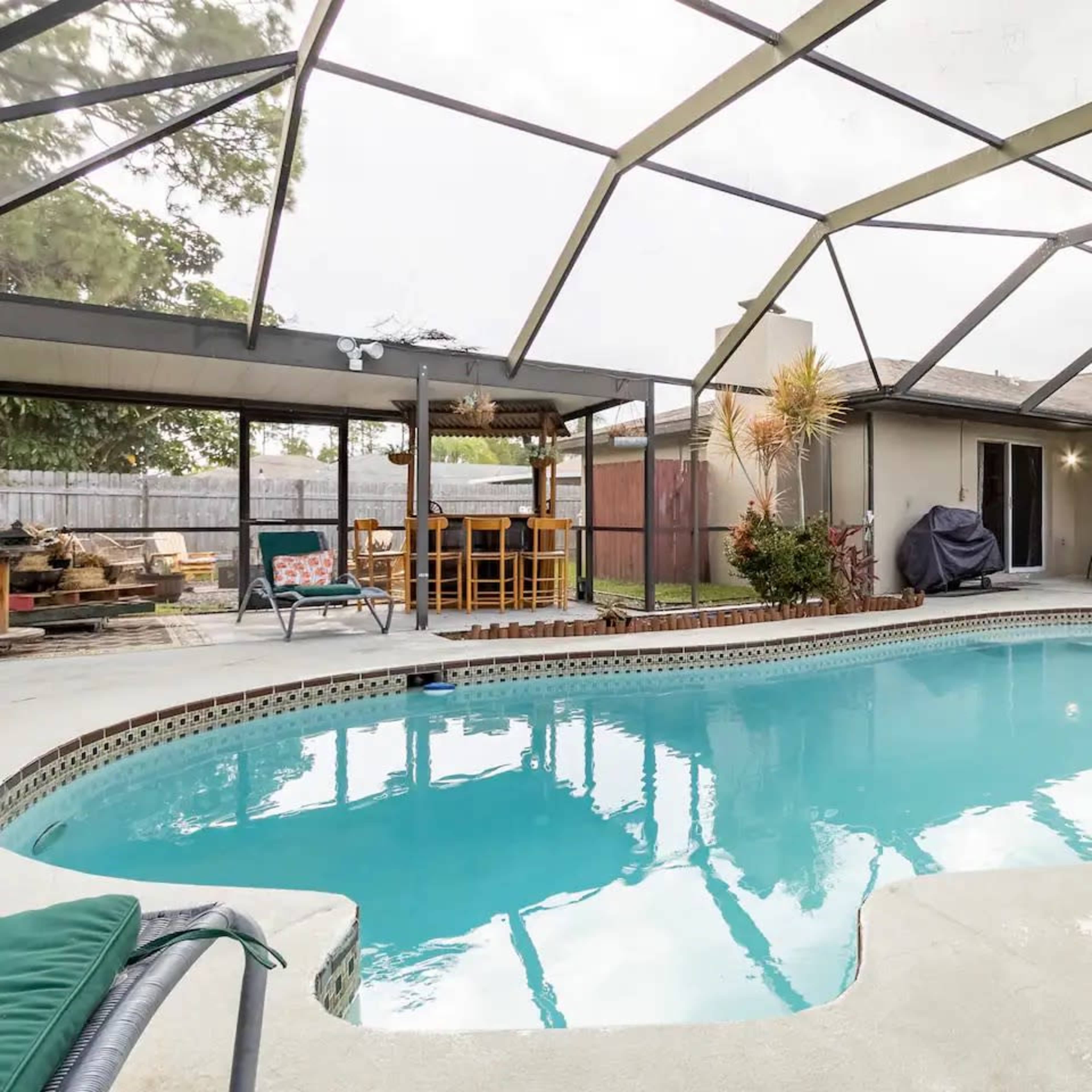 A swimming pool surrounded by a screened enclosure and outdoor furniture in a residential backyard.
