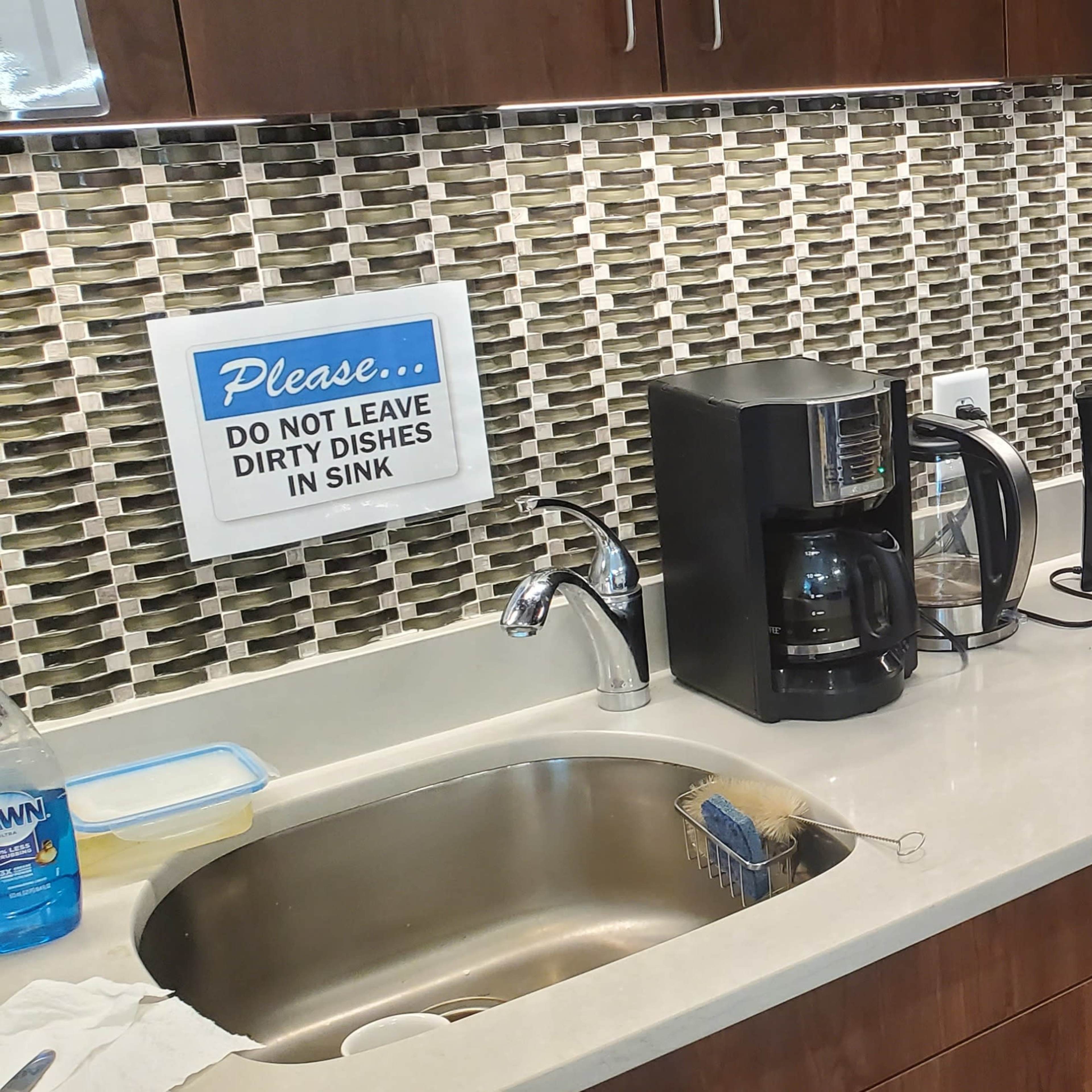 A kitchen countertop with a sink, coffee maker, microwave, and a canister on top, against a tiled backsplash.