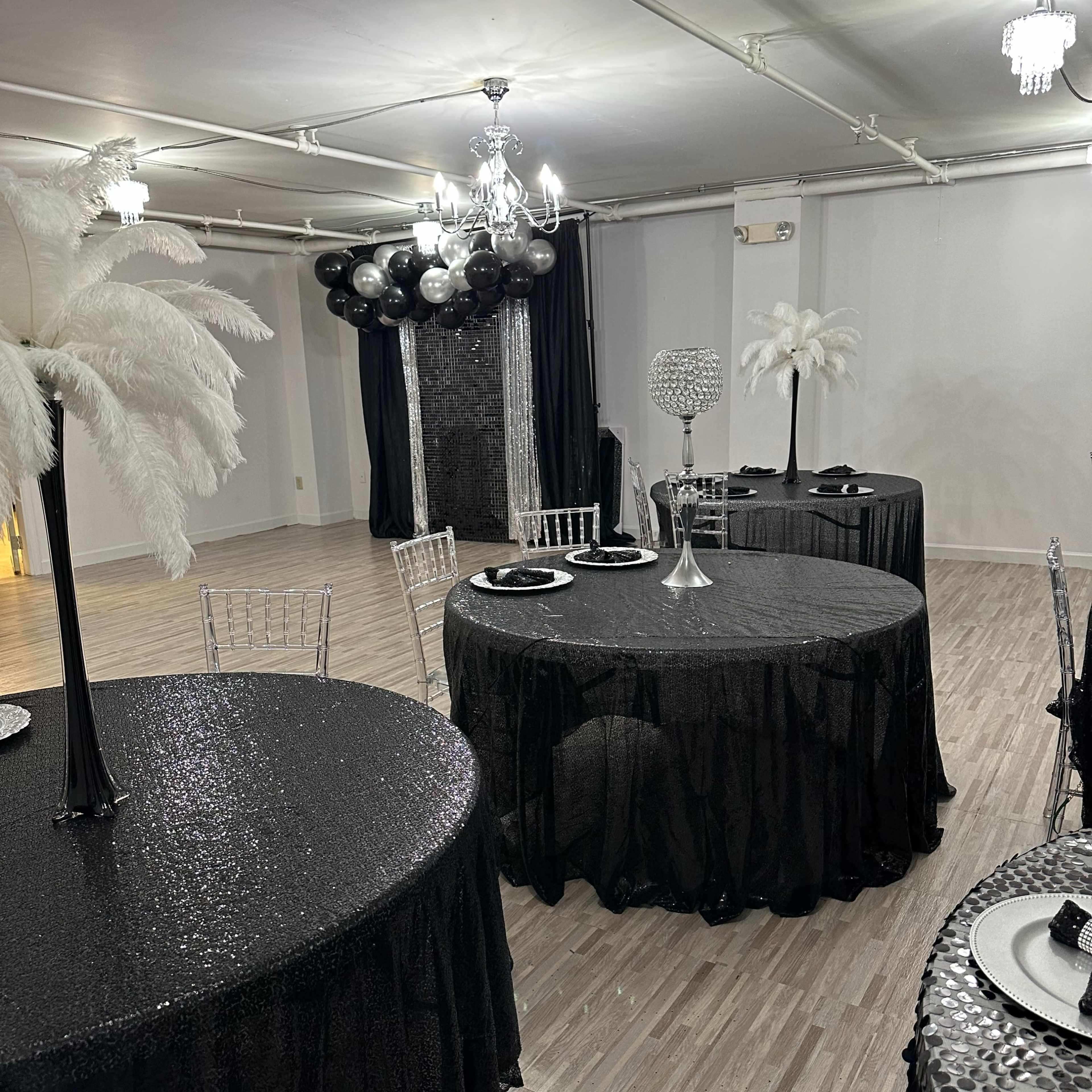 A banquet hall decorated with black and white tables, featuring feather centerpieces and elegant tableware.