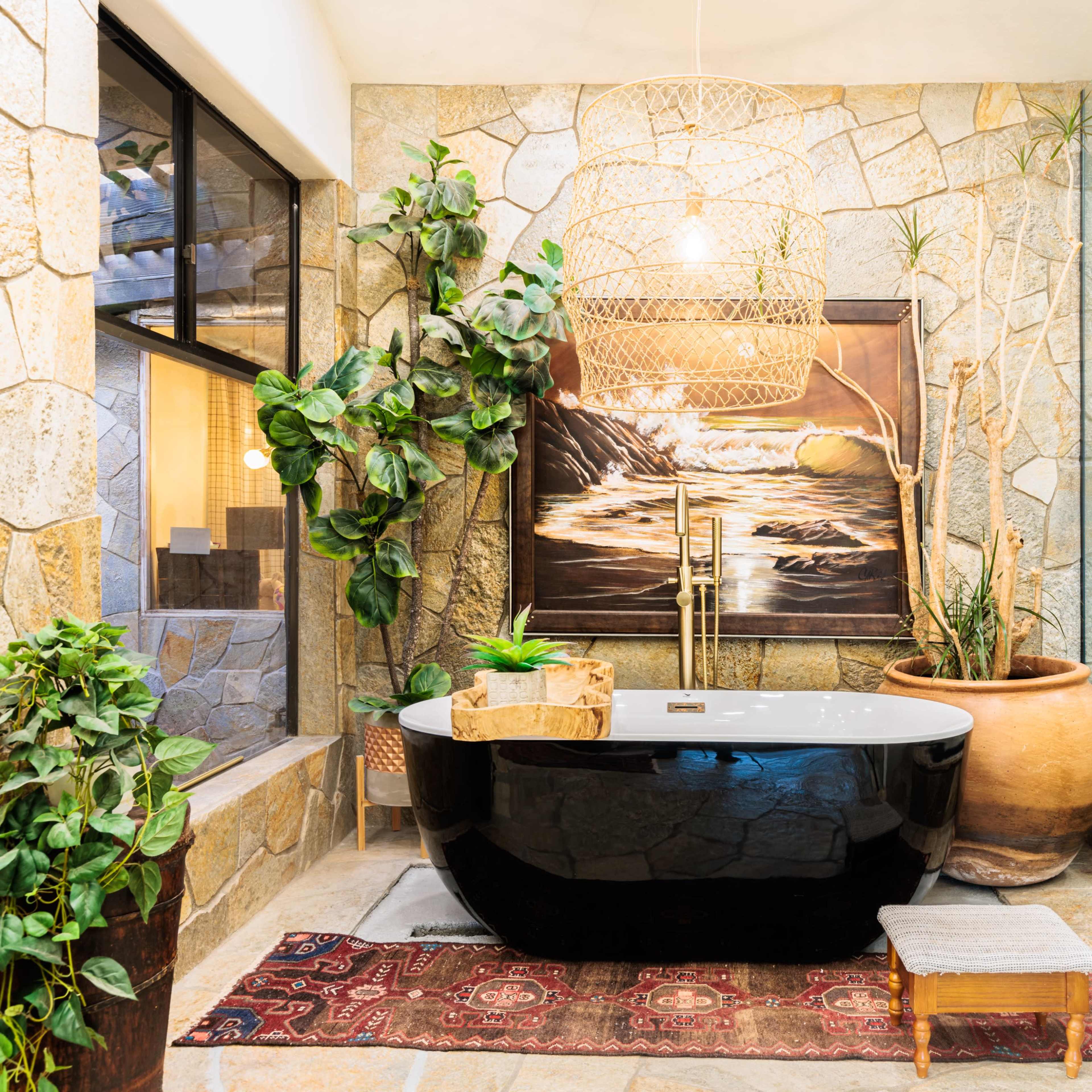 A modern bathroom featuring a black freestanding bathtub, stone walls, and a glass shower enclosure, accented by greenery and decorative elements.
