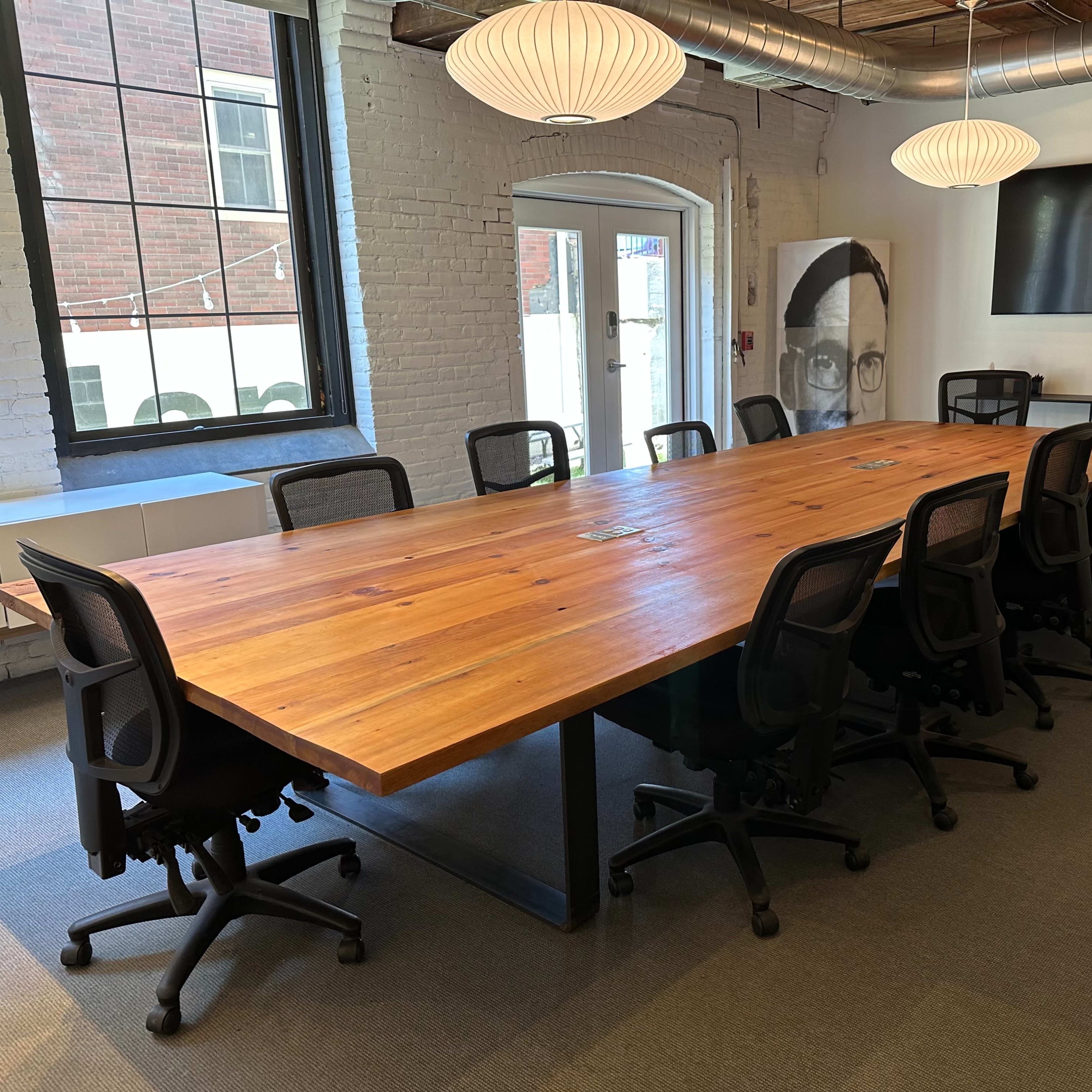 A large wooden conference table surrounded by black office chairs in a modern meeting room.