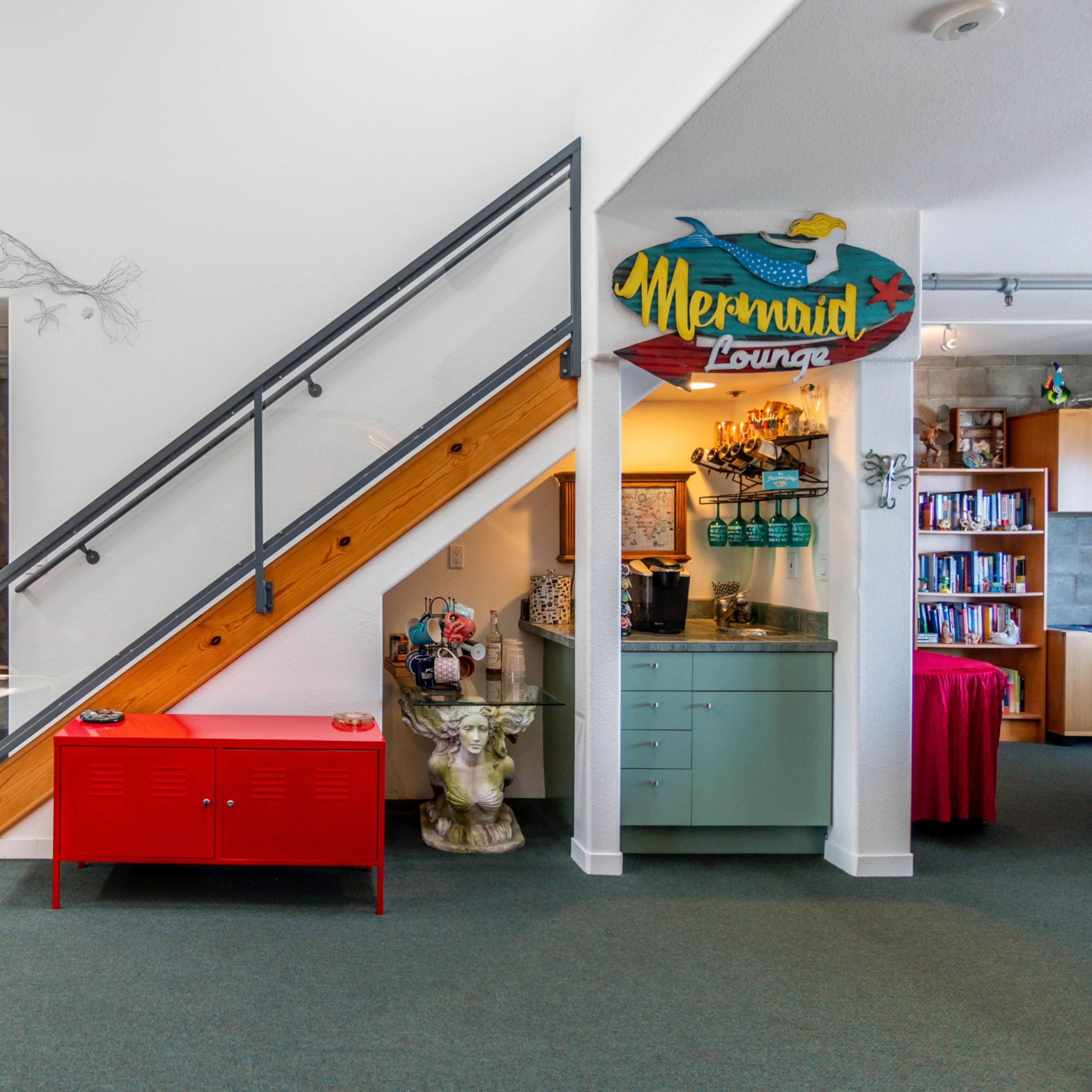 A brightly lit interior space featuring a staircase on the left, a red cabinet, and a decorated wall labeled "Mermaid Lounge."