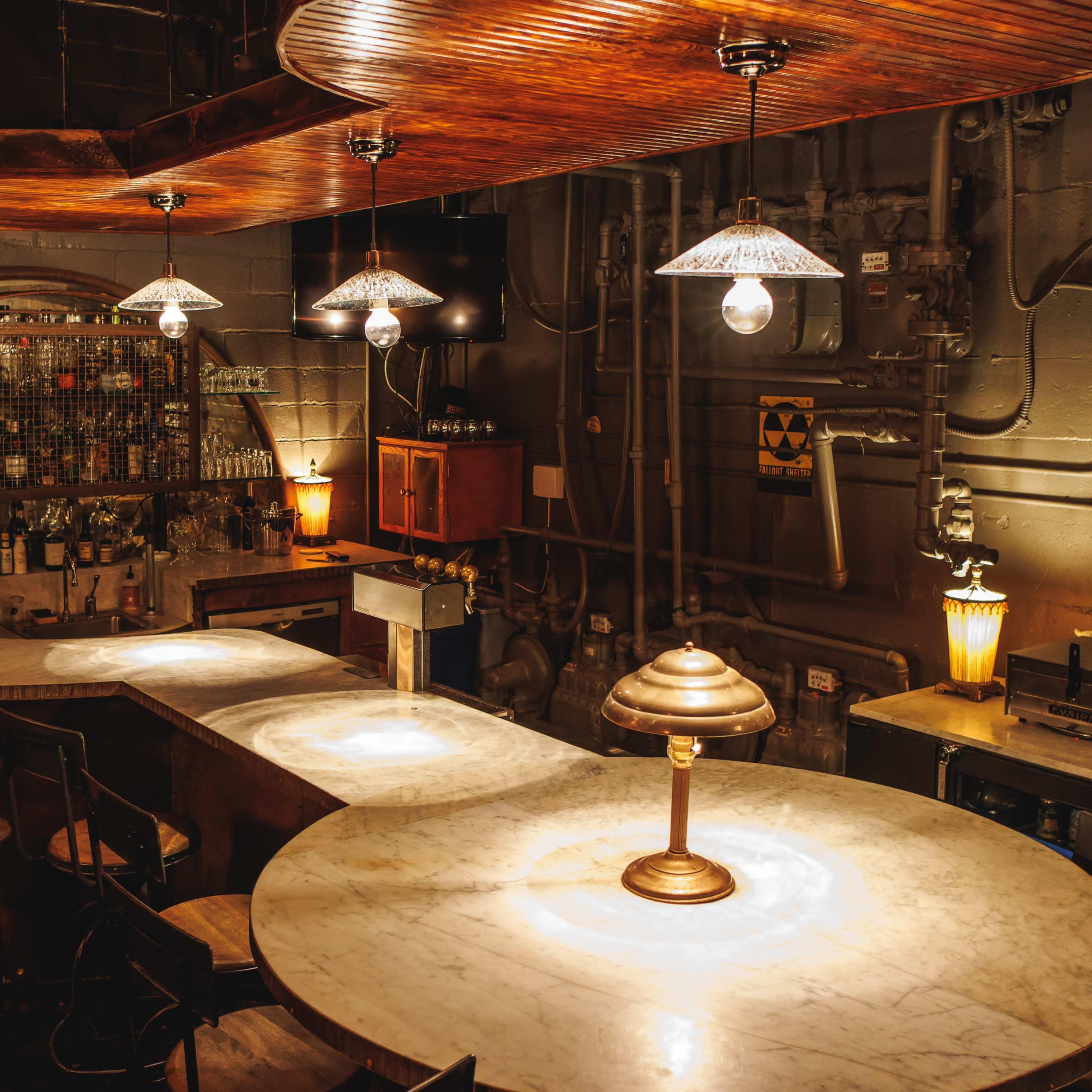 A dimly lit bar features a white marble countertop, wooden accents, and vintage lamps hanging above.