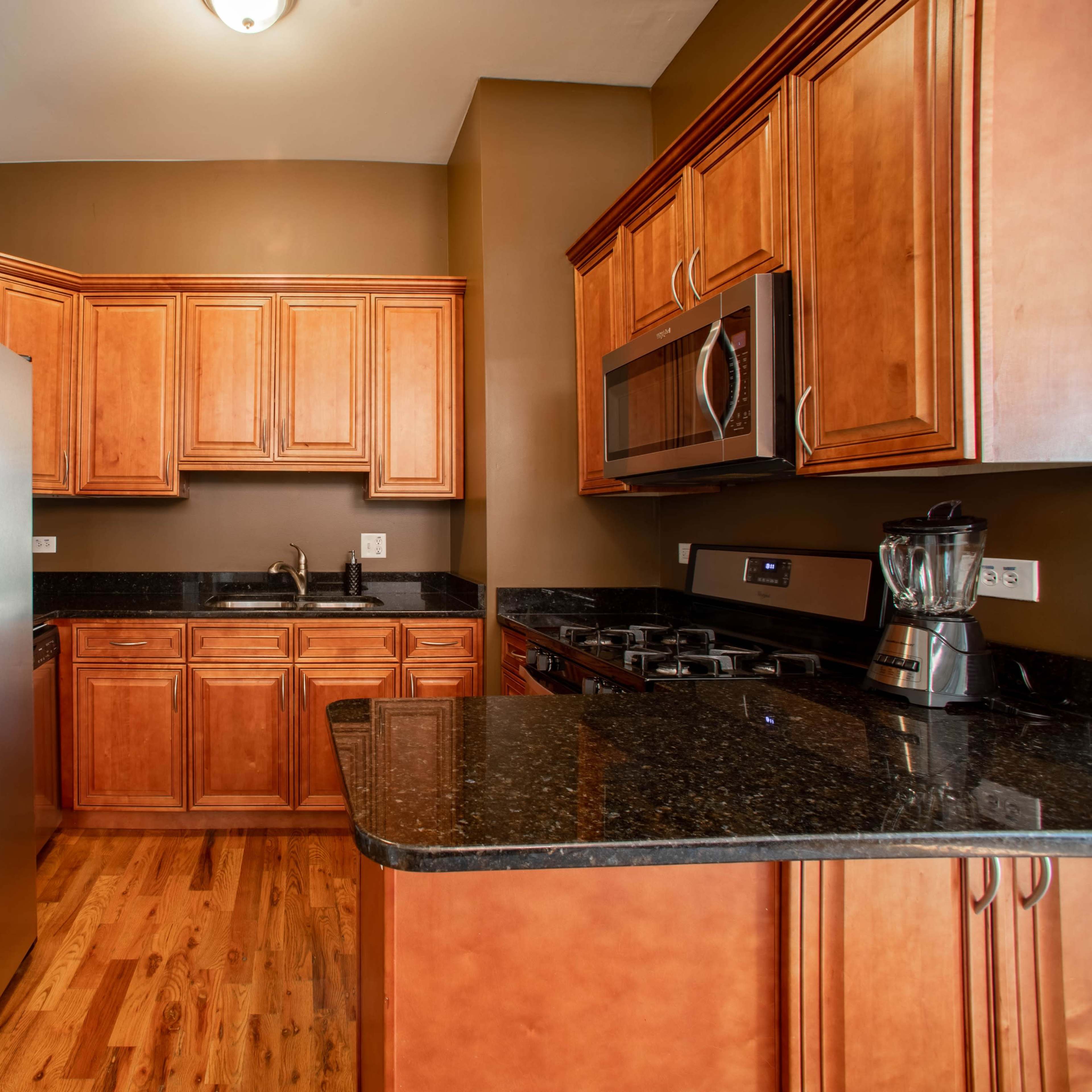 A modern kitchen featuring wooden cabinetry, a stainless steel refrigerator, a black countertop, and integrated appliances.