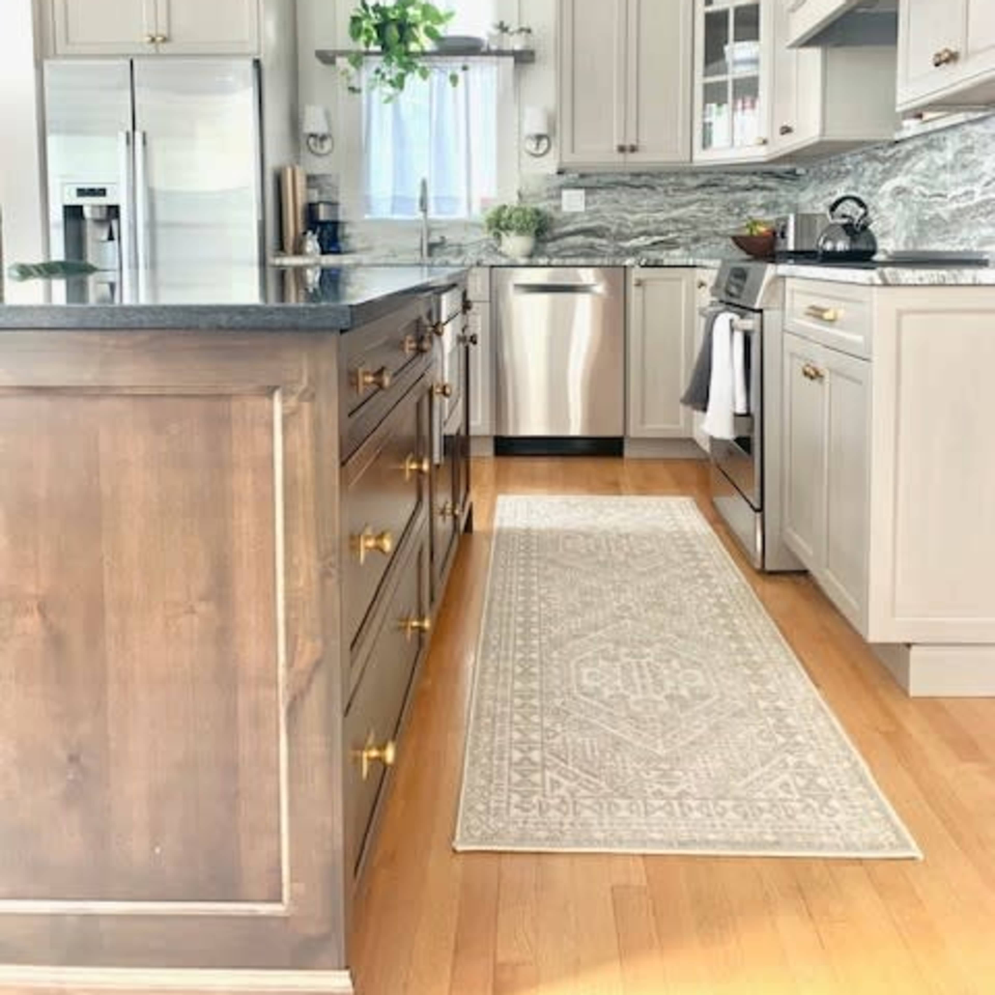 A modern kitchen featuring light gray cabinetry, a marble backsplash, stainless steel appliances, and a decorative area rug on a hardwood floor.