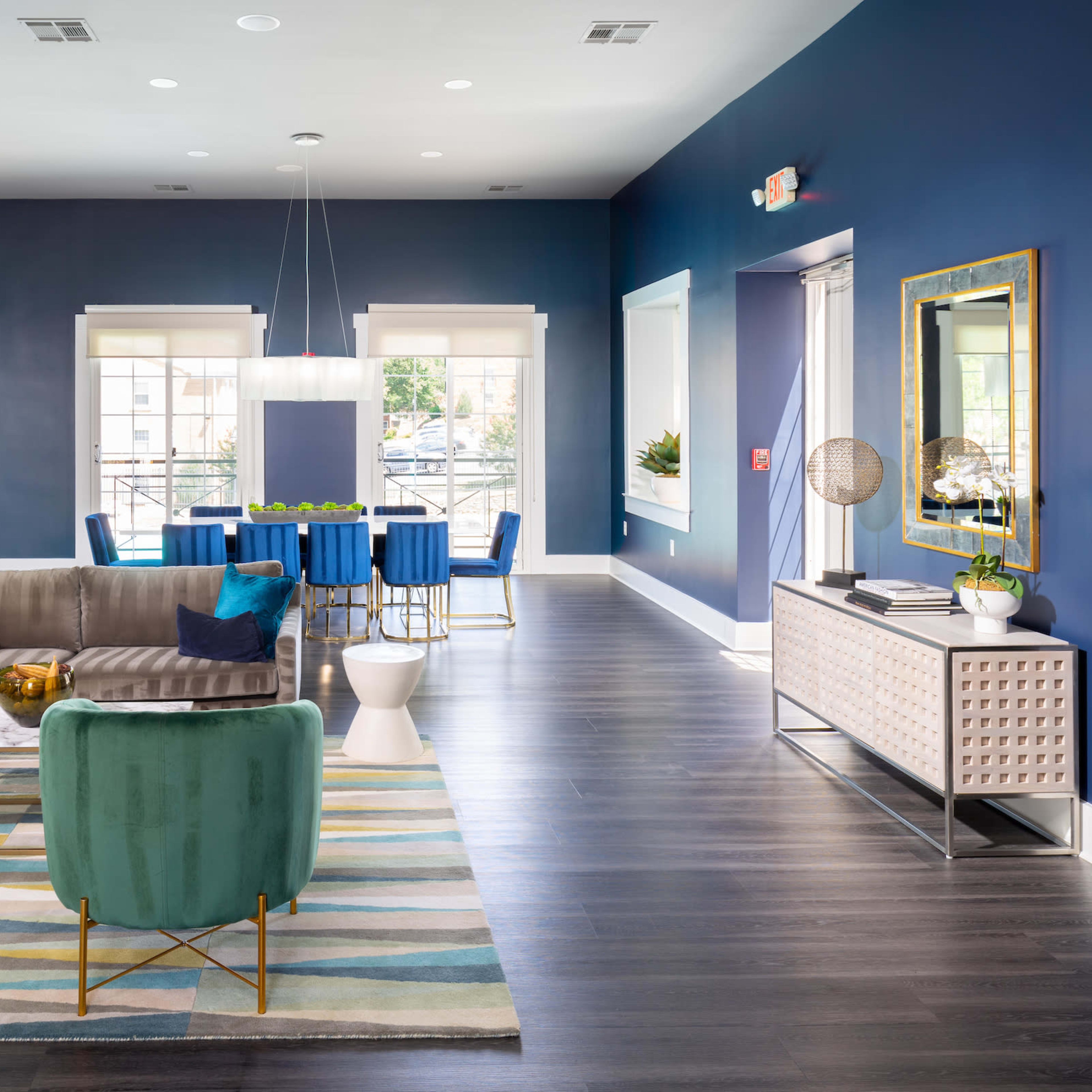 A modern living space featuring a seating area with green chairs, a gray sofa, a patterned rug, and a dining area with blue chairs against a dark blue wall.