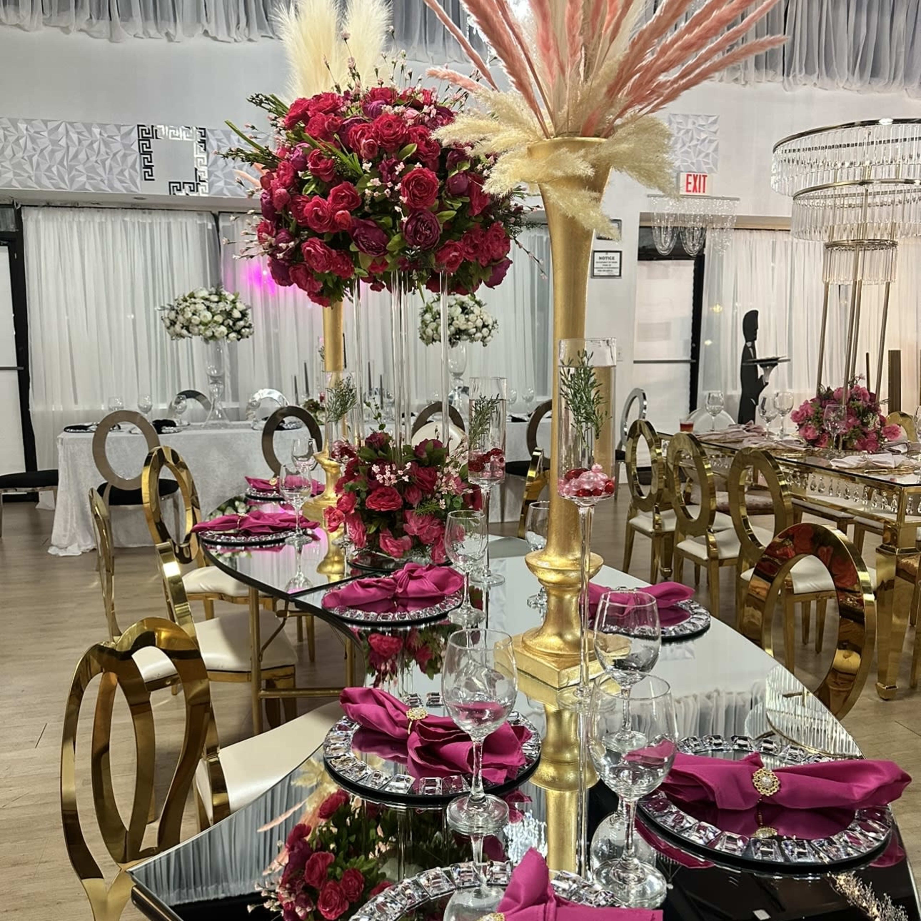 A beautifully arranged dinner setting with tall floral centerpieces, gold-accented tableware, and elegantly folded pink napkins on mirrored tables.