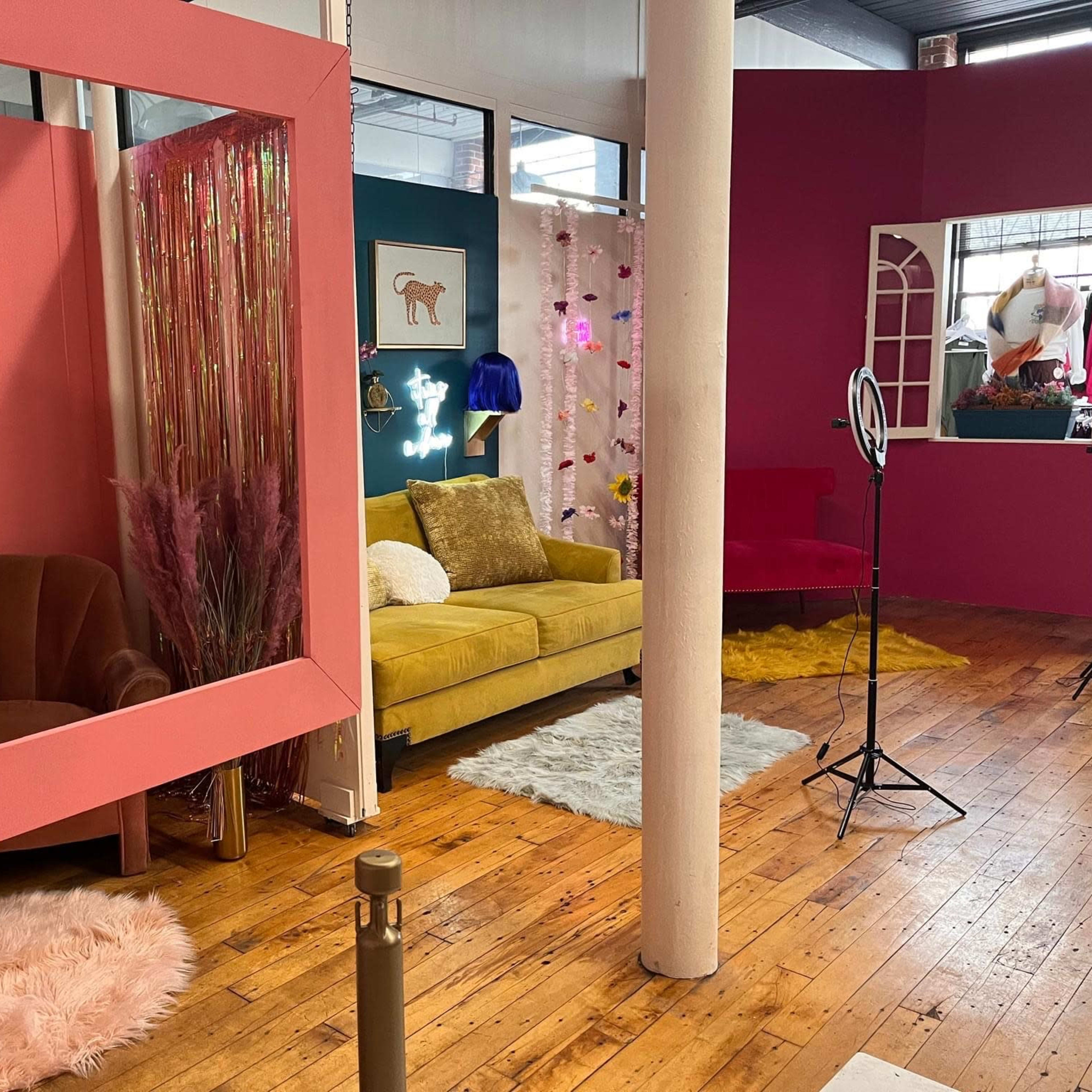 A colorful interior space featuring a pink accent wall, a yellow sofa, decorative mirrors, and various textures on the floor.