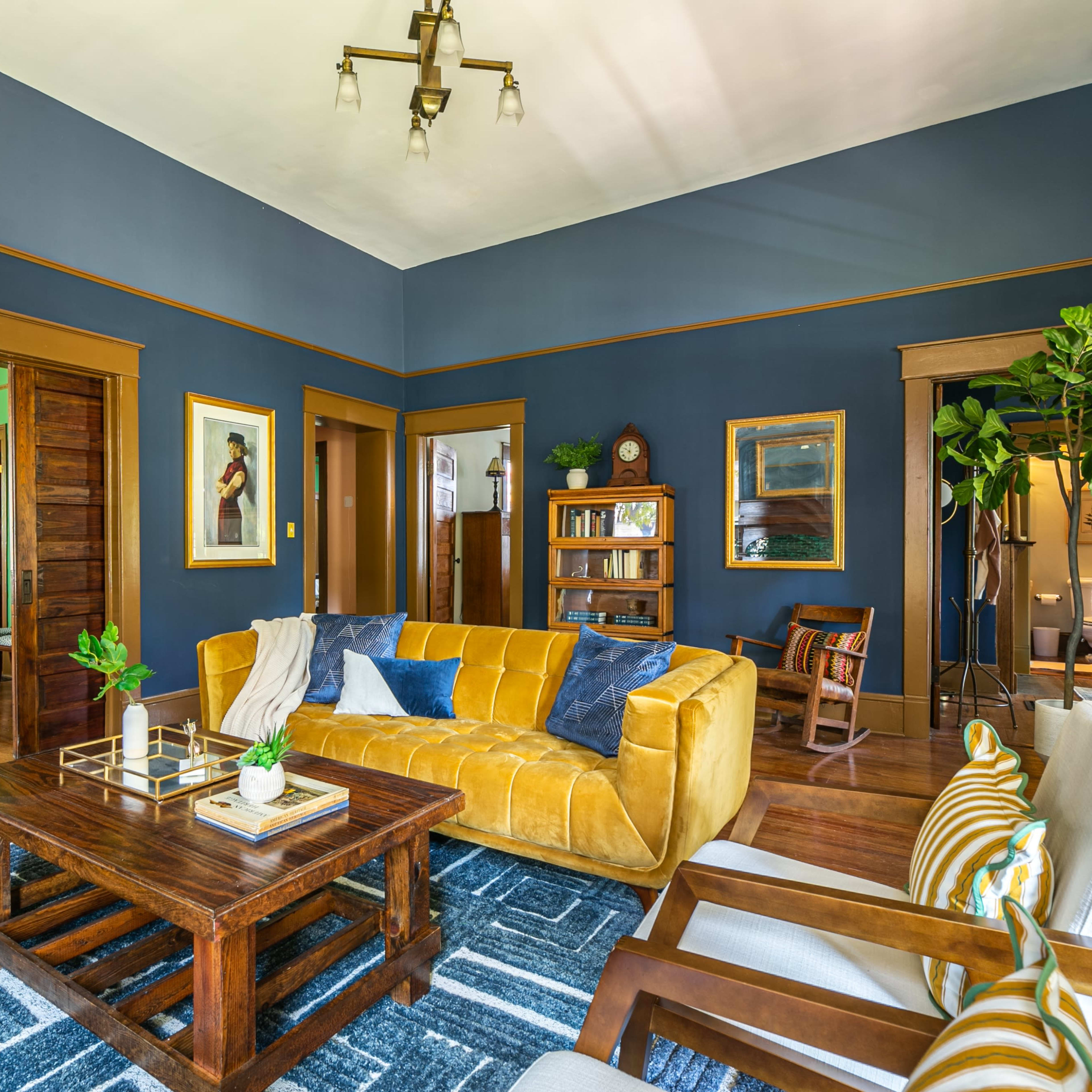 A living room with a yellow sofa, a wooden coffee table, and a blue wall, showcasing doorways leading to adjacent rooms.