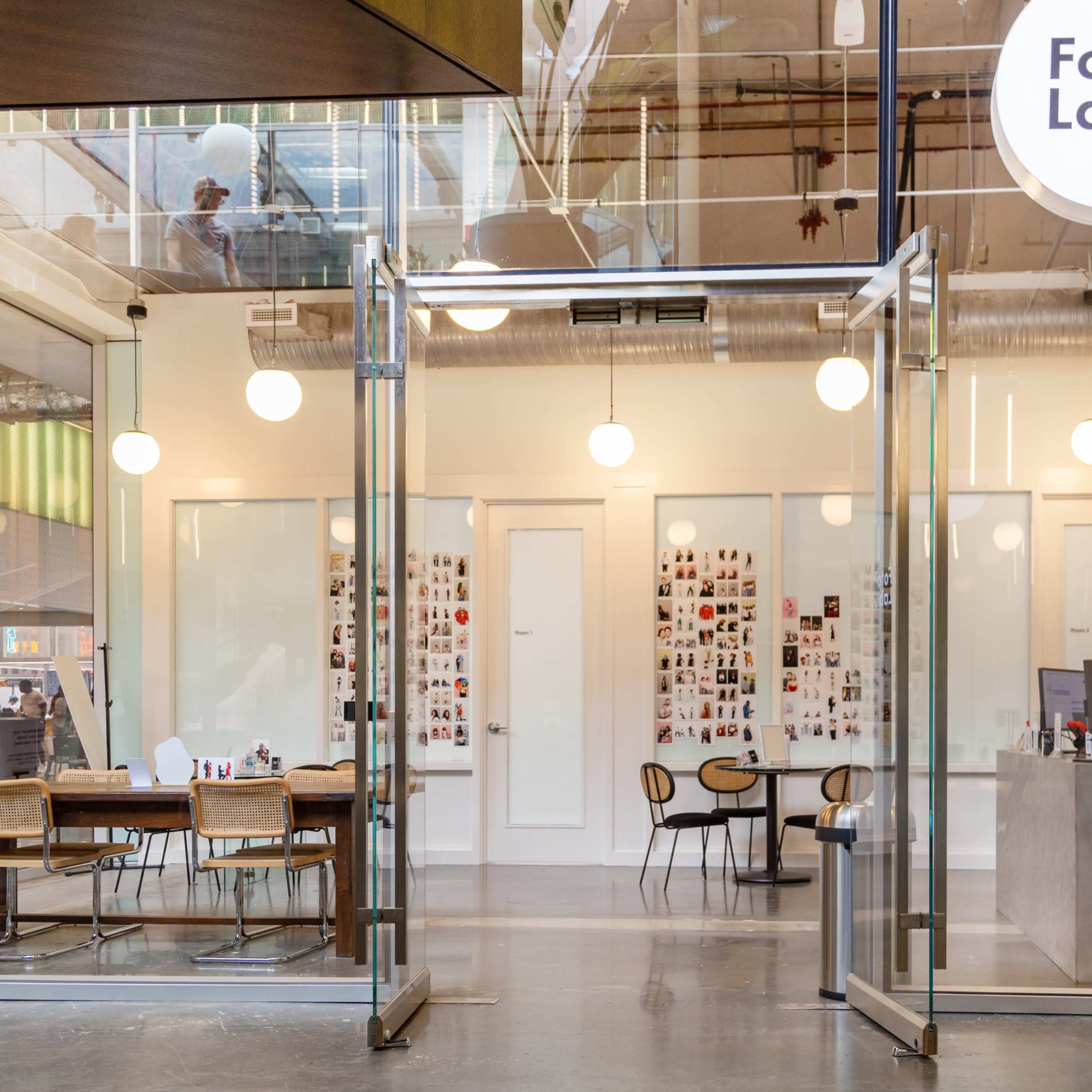 The entrance of a modern photo lab with large glass doors, displaying a bright interior that includes tables and a counter.