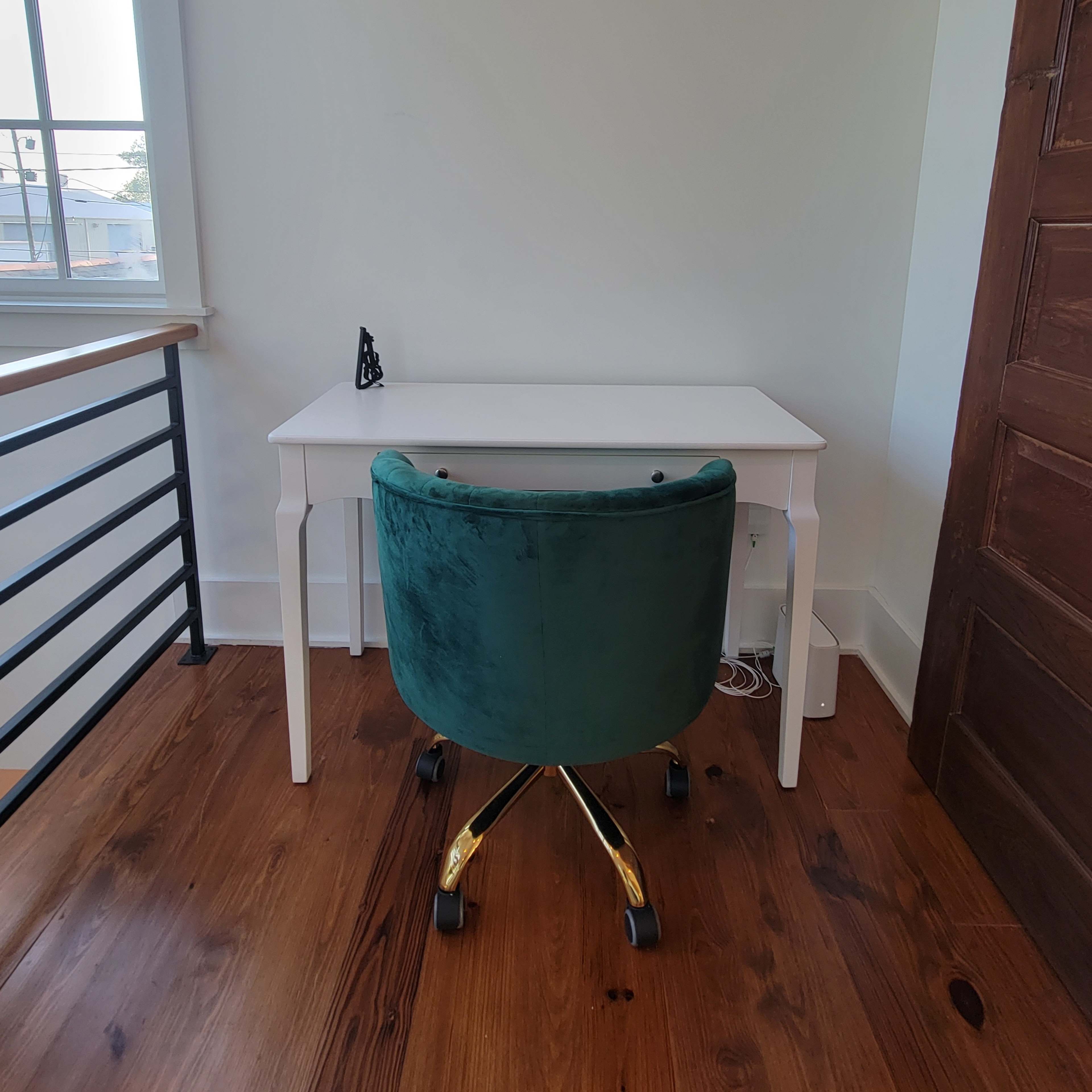 A small white desk with a green upholstered chair positioned in a corner of a room with wooden flooring.