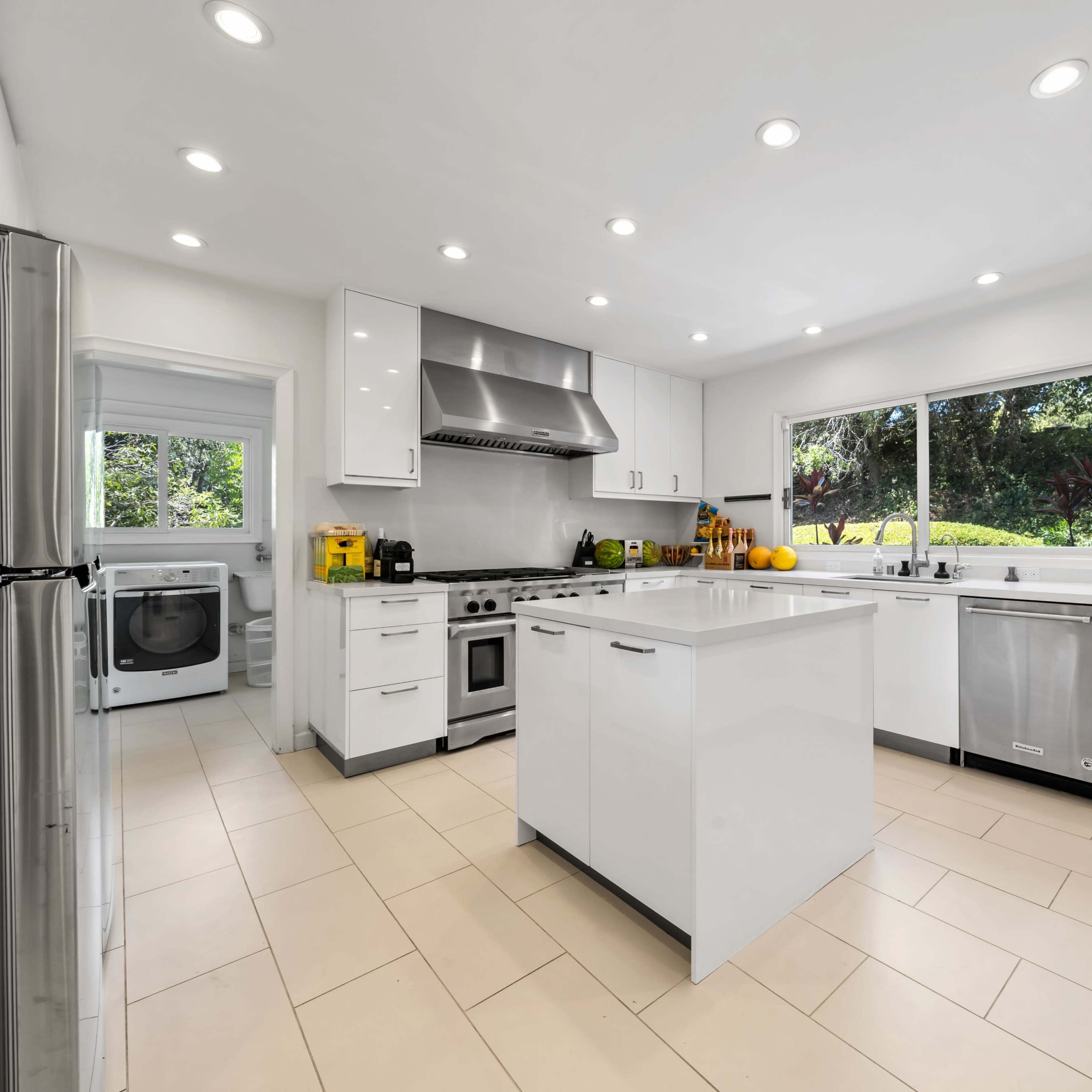 A modern kitchen features white cabinetry, stainless steel appliances, and an island with a sink, illuminated by recessed lighting.