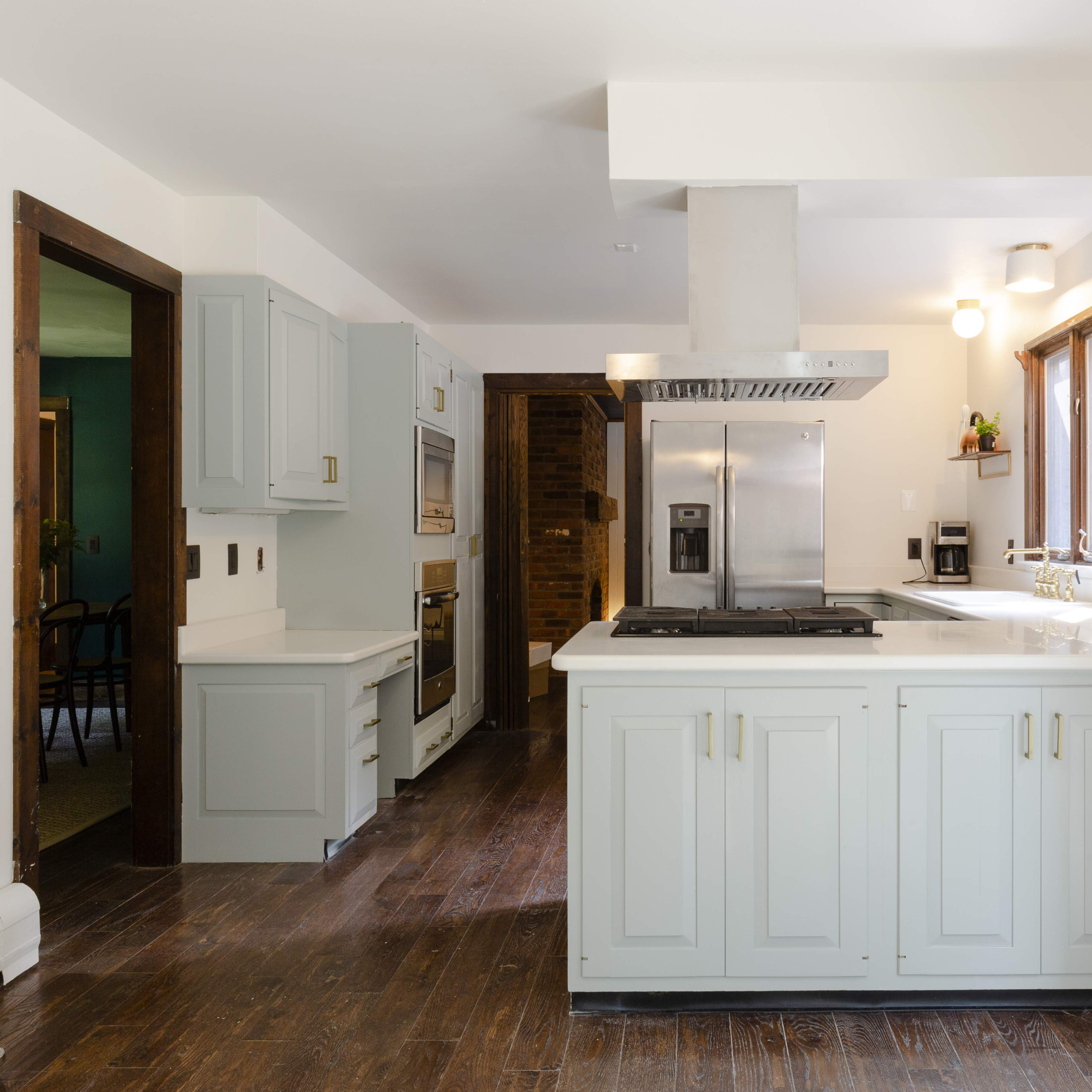A modern kitchen features light green cabinetry, stainless steel appliances, and a central island with a gas cooktop.