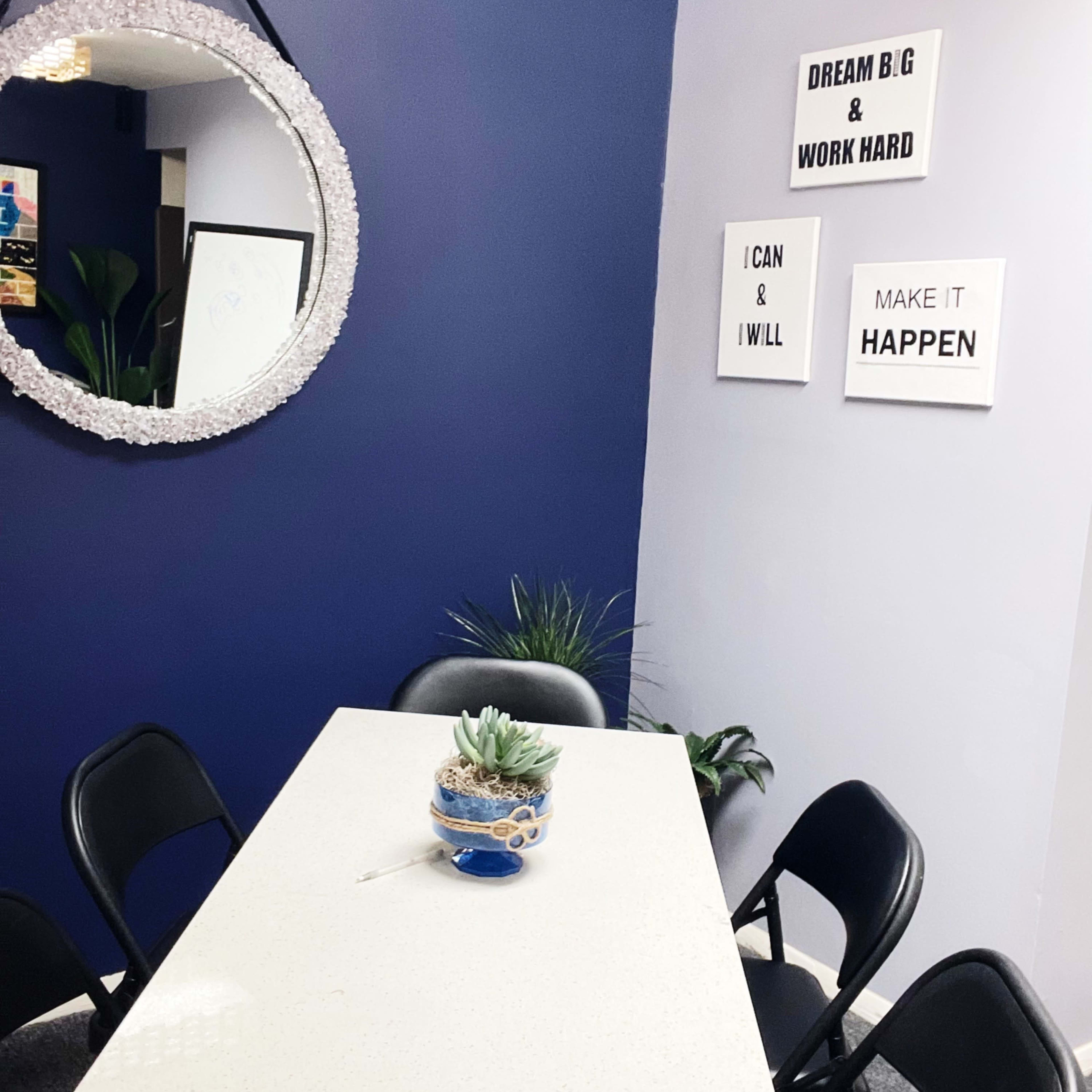 A small dining area features a circular mirror on the wall, a white table surrounded by black chairs, and motivational art on the purple wall.