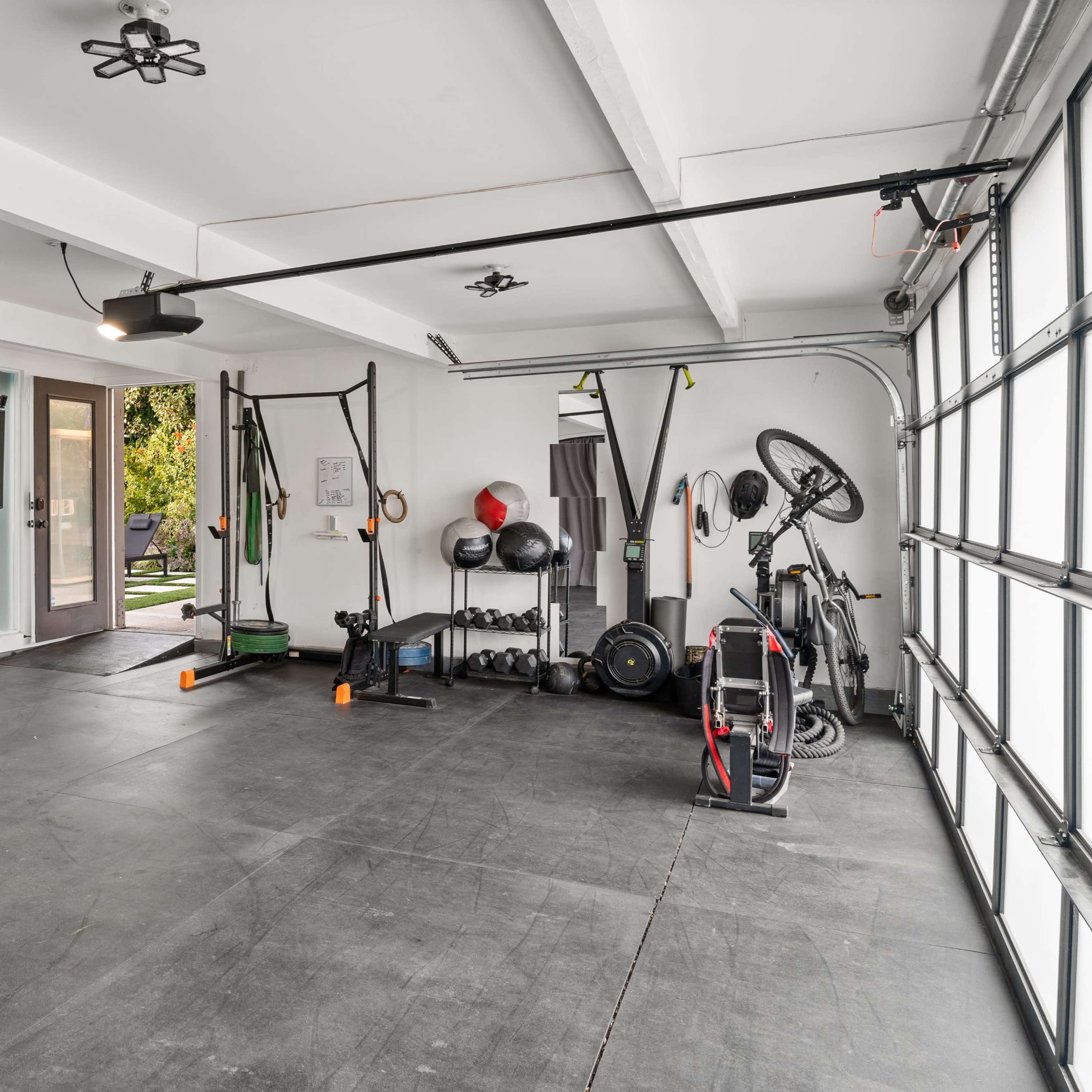 A spacious garage converted into a home gym, featuring exercise equipment, a chair, and a large glass garage door.