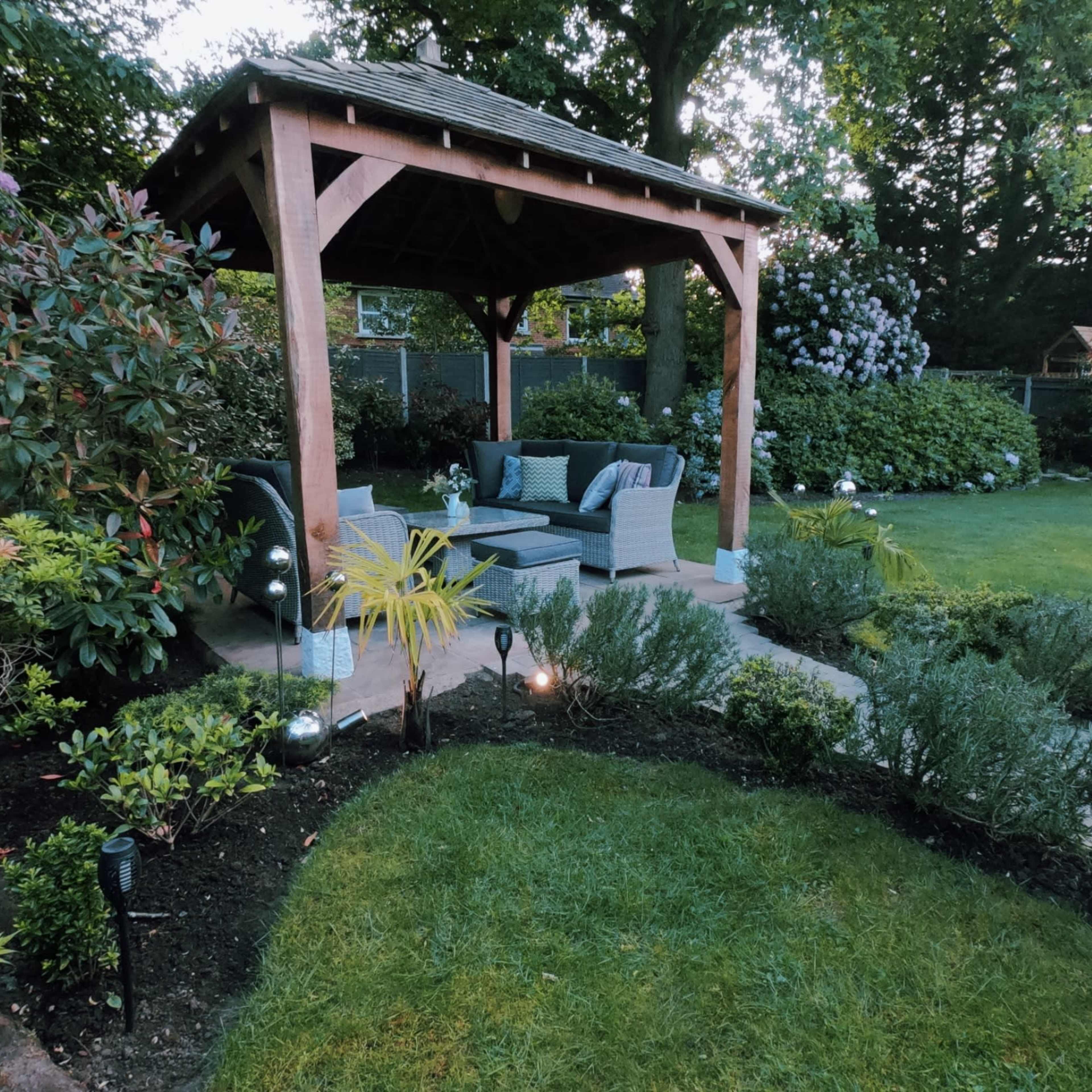A garden with a gazebo featuring seating, surrounded by greenery and landscaped flower beds.
