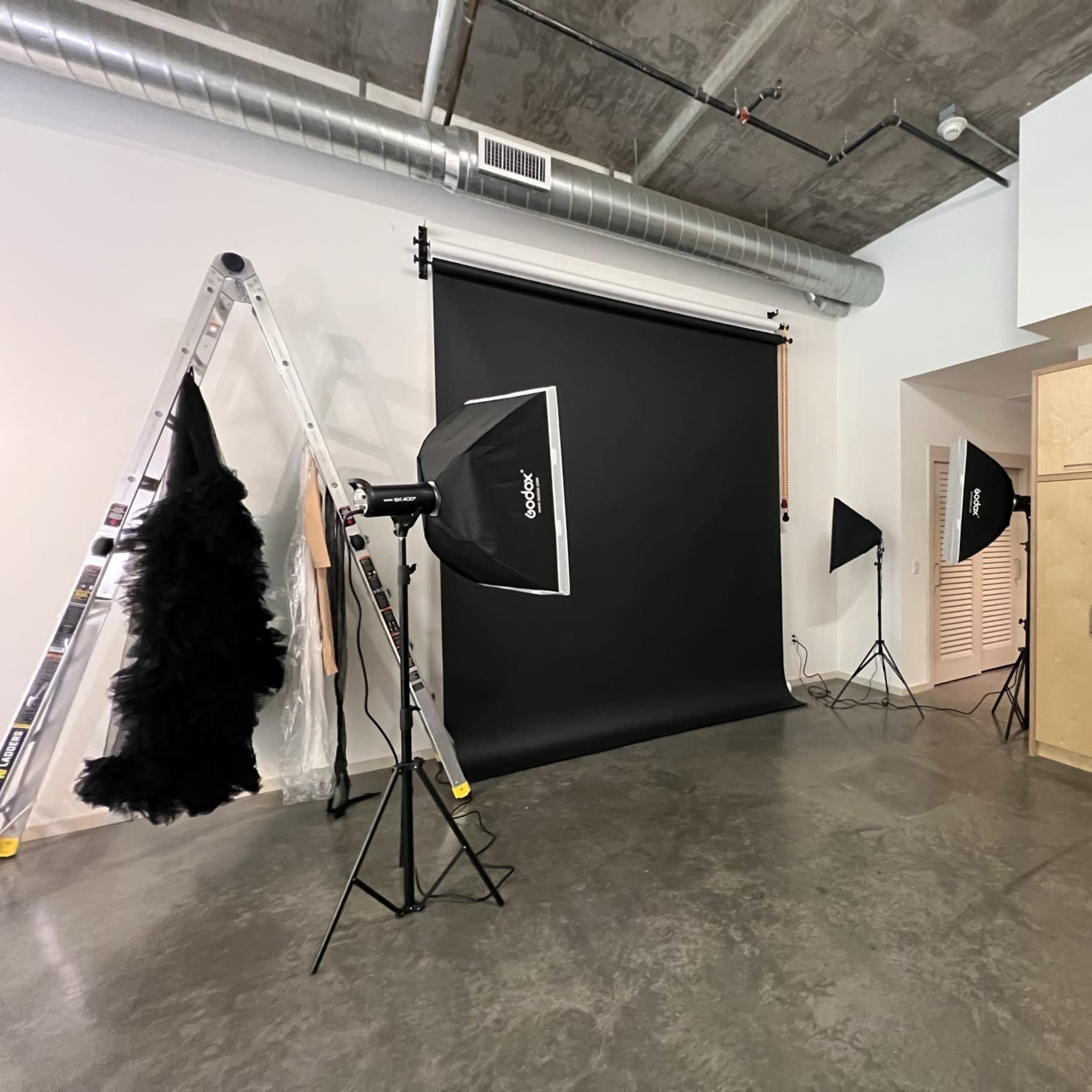 A photography studio with a black backdrop, several lighting setups, a ladder, and a garment rack displaying a costume.