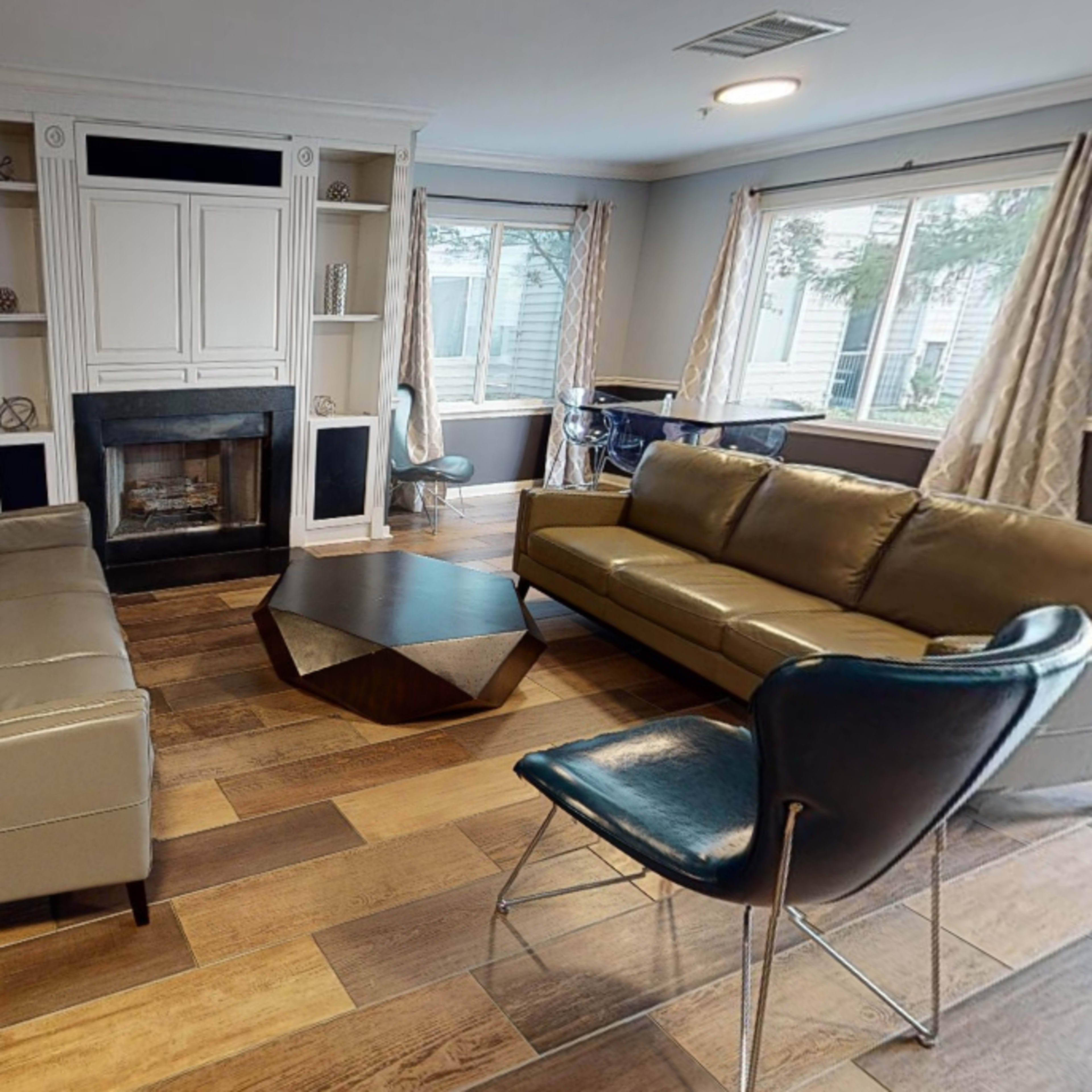 A living room with two sofas, a coffee table, and a fireplace, surrounded by windows and a blue chair.