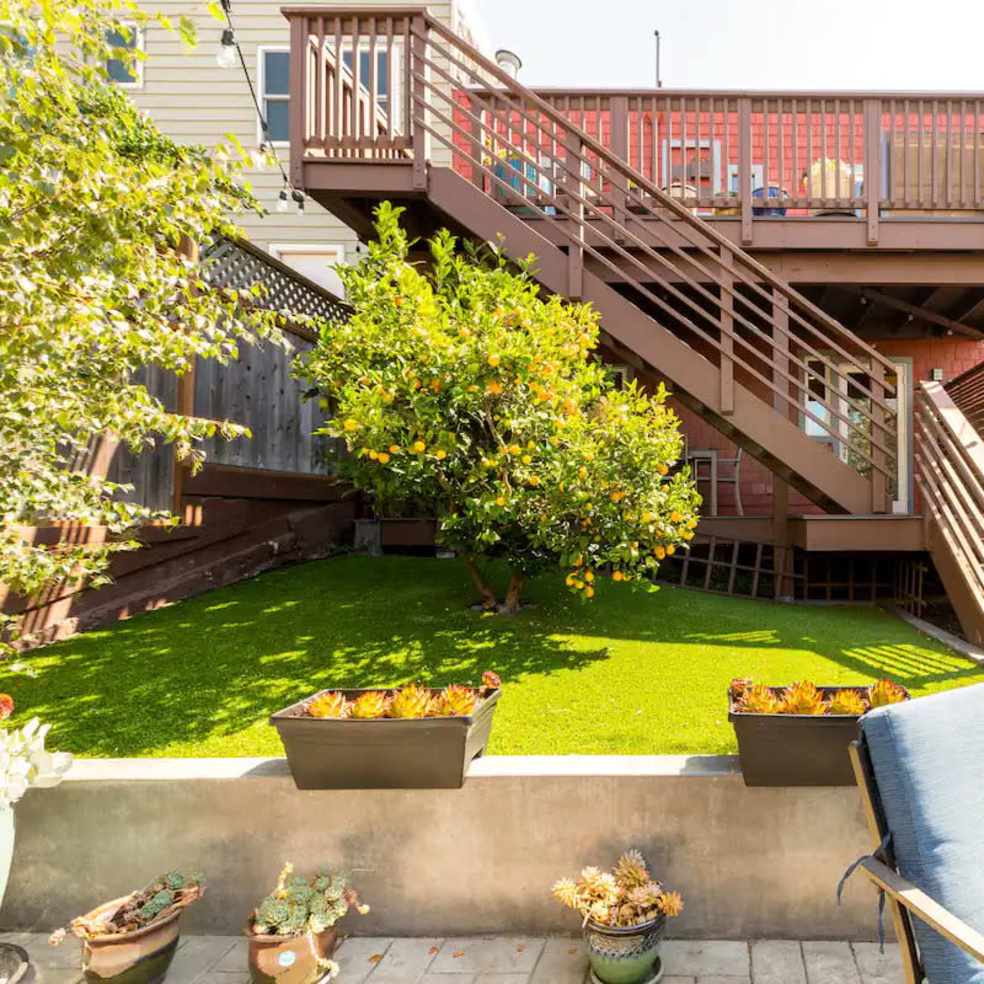 A backyard with a multi-level wooden deck, a green lawn, and potted plants along a stone pathway.
