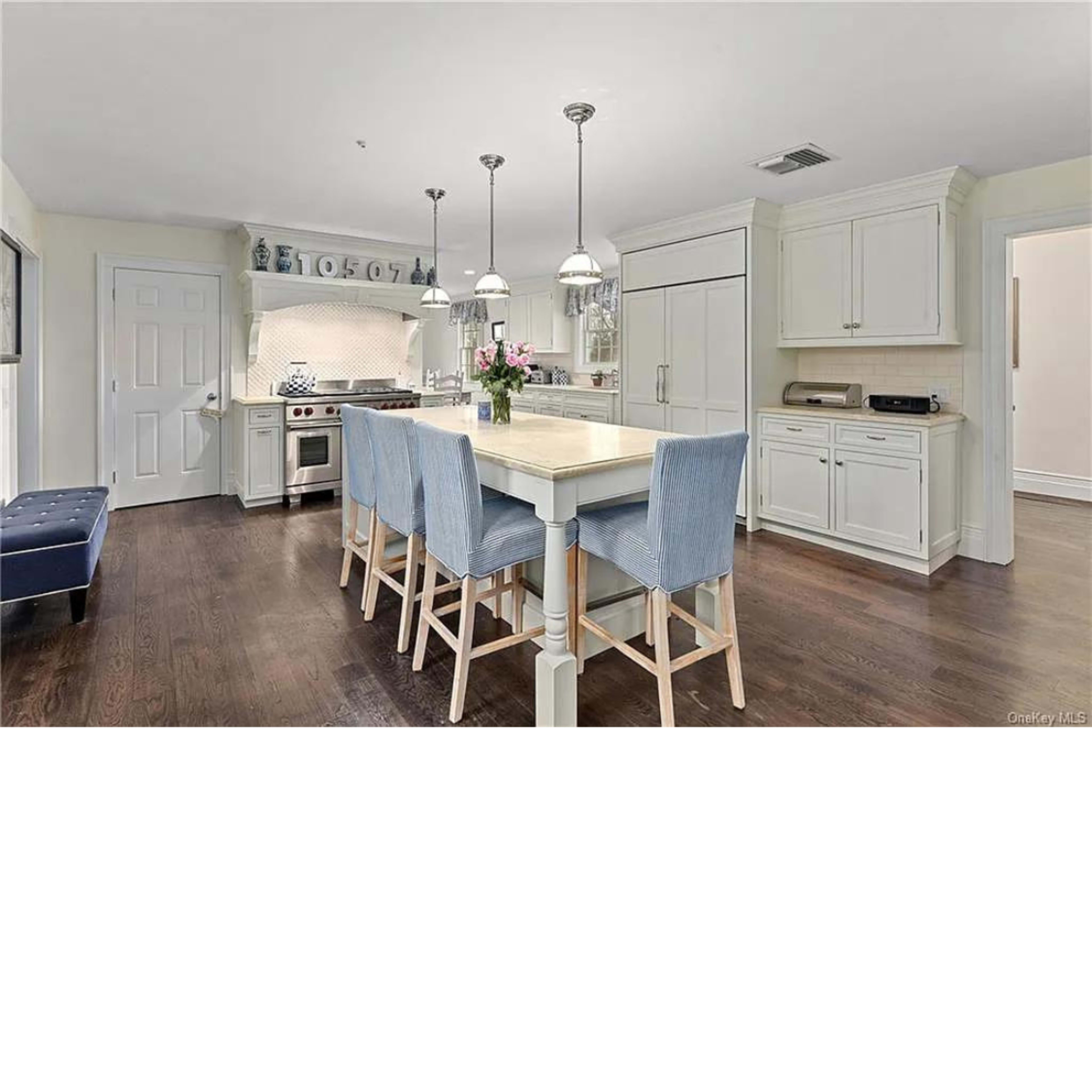 A modern kitchen features a central island with bar seating, light cabinetry, and stainless steel appliances.