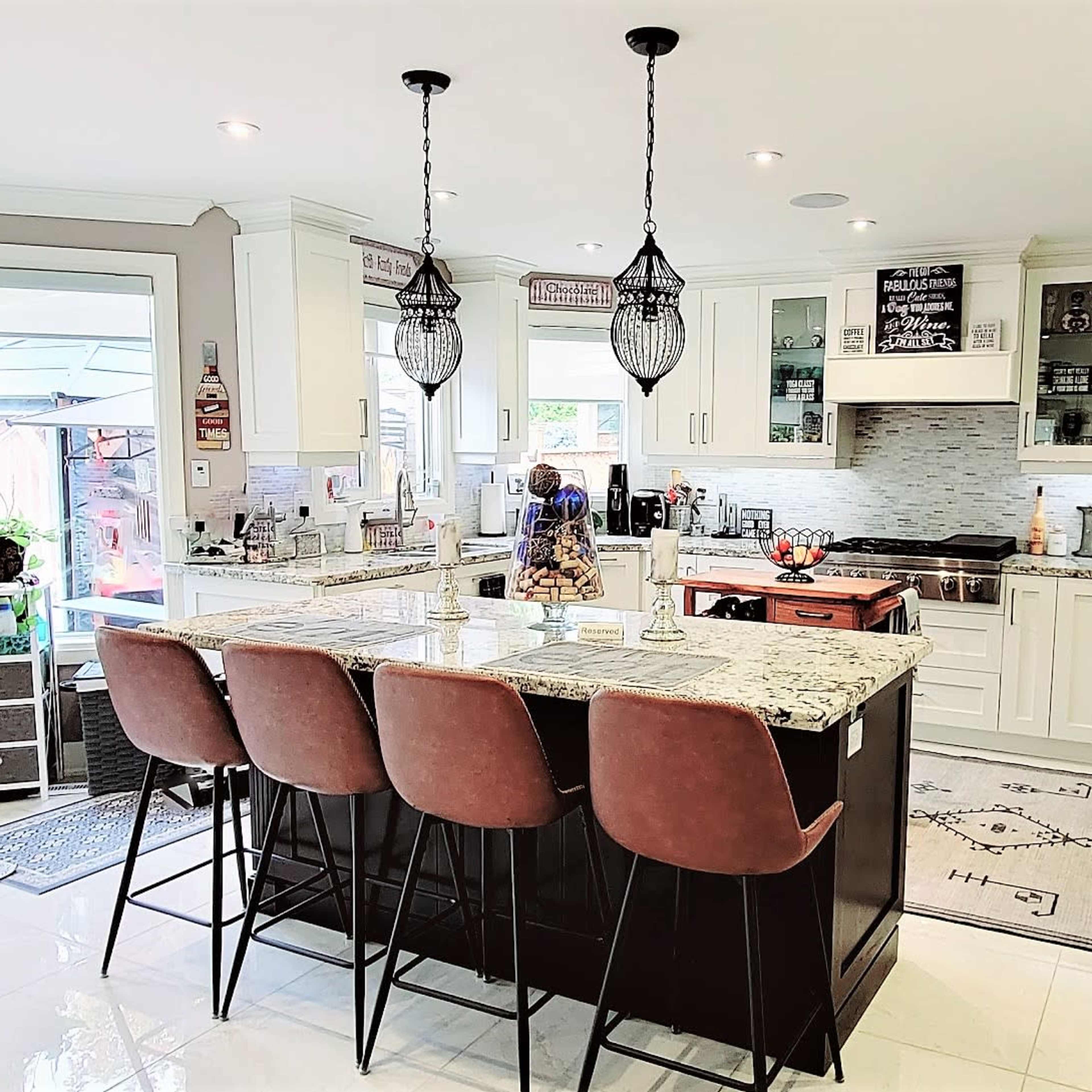 A modern kitchen features a central island with bar seating, white cabinetry, and stainless steel appliances.