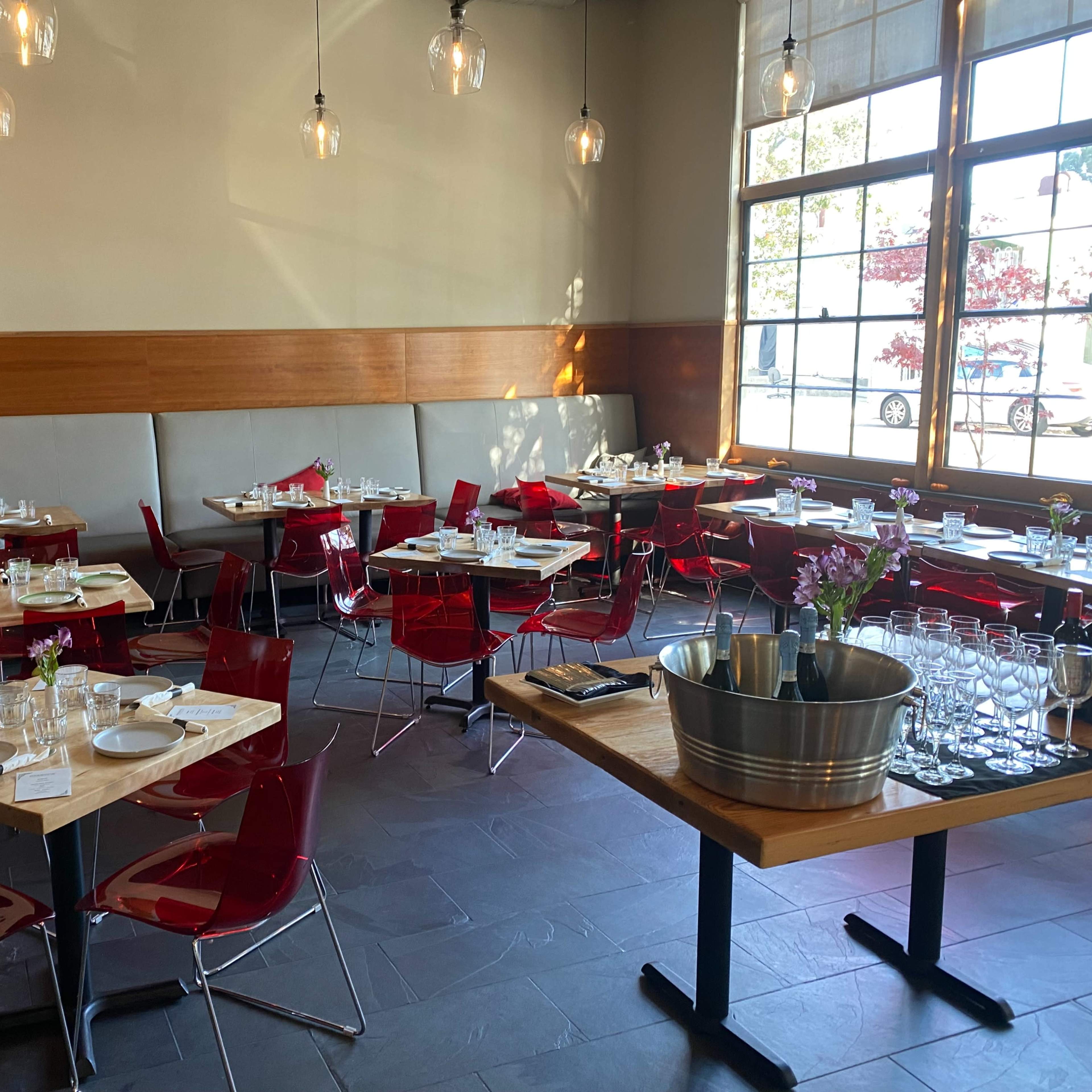 An indoor restaurant setting with red chairs and tables arranged neatly, featuring glassware and table settings on each table.