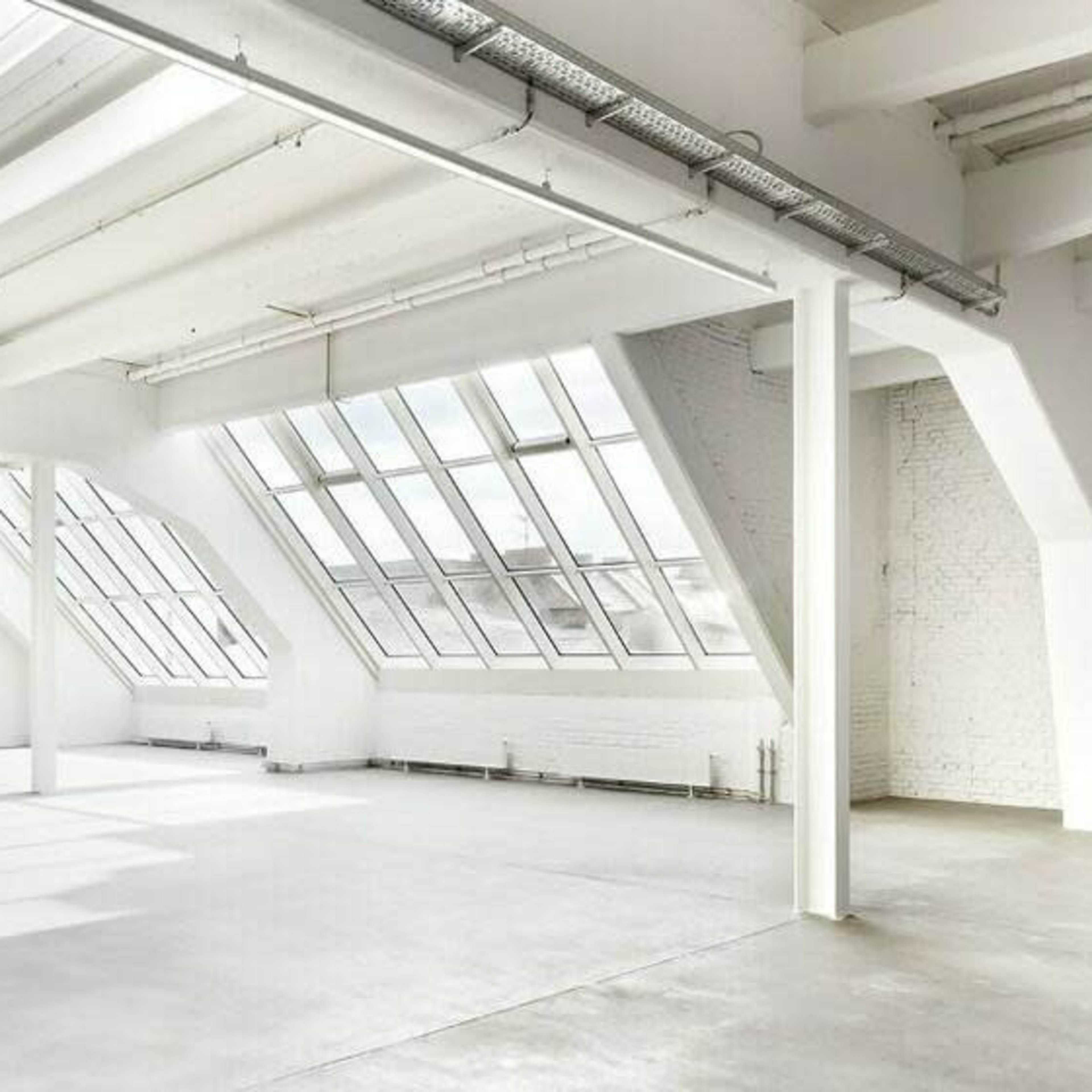 A spacious, well-lit interior of an industrial-style building with large windows and an open floor plan.