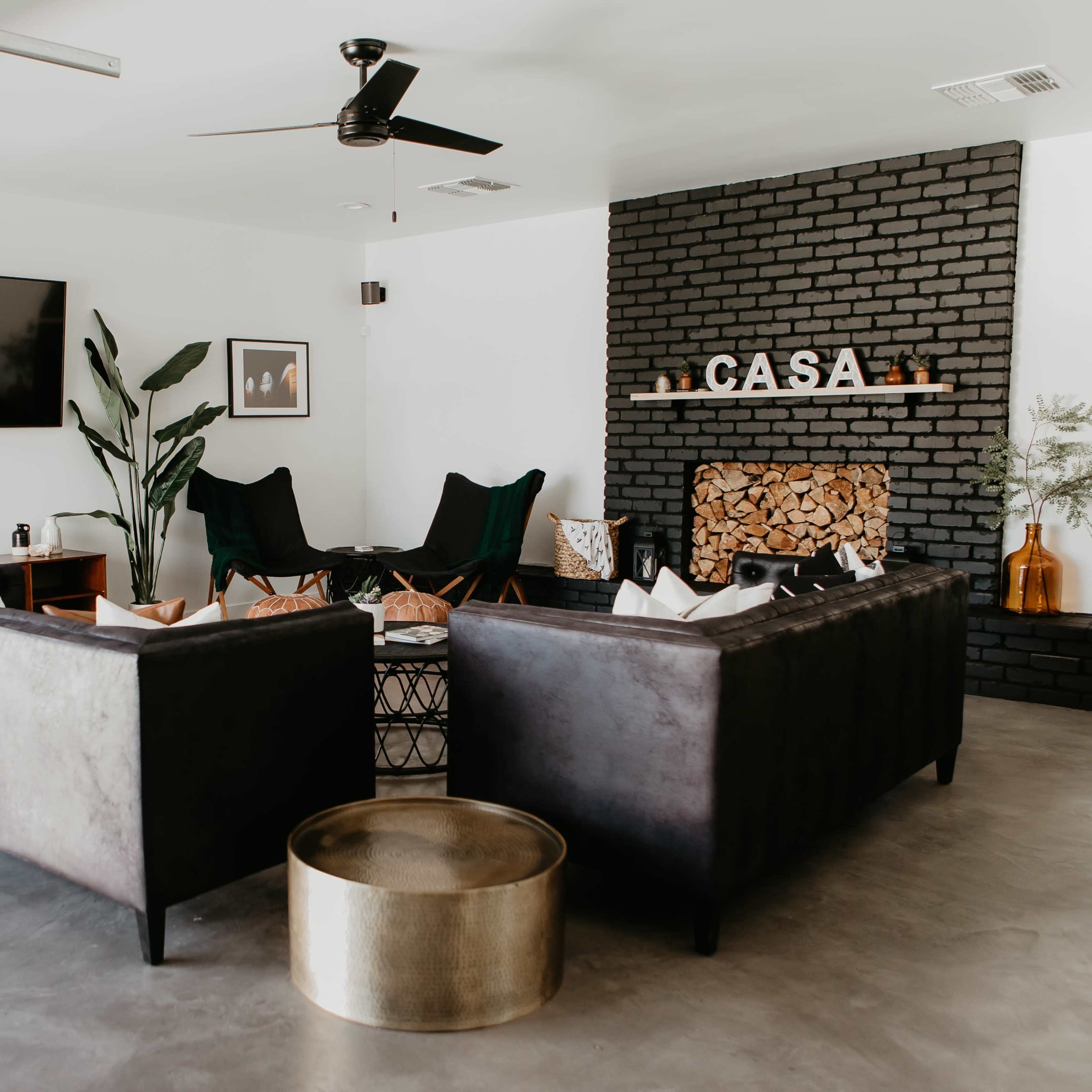 A modern living room features two dark couches facing each other, a coffee table in the center, a wall-mounted TV, and a decorative fireplace with the word "CASA" above it.
