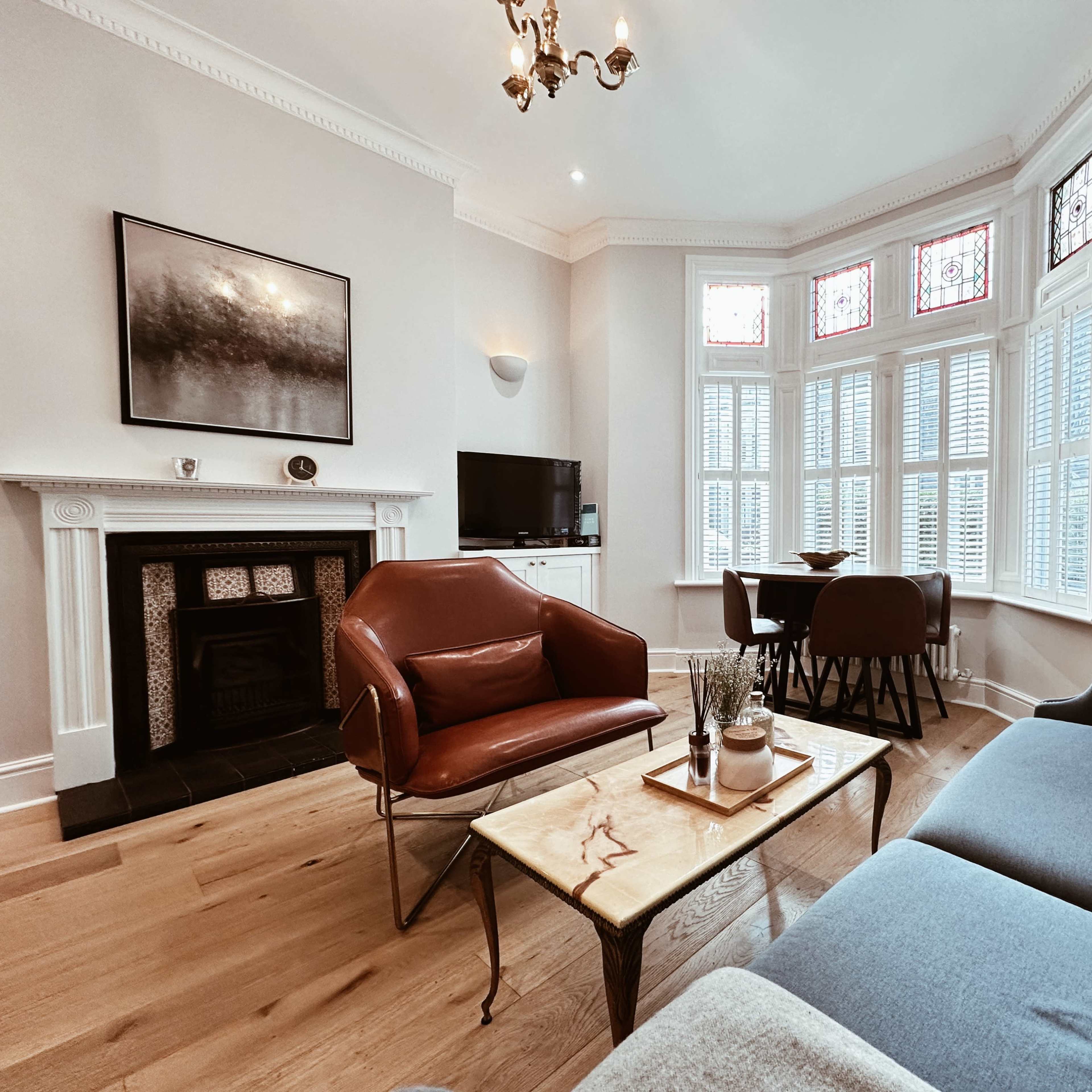A bright living room featuring a blue sofa, a brown armchair, a wooden coffee table, and a bay window with stained glass.