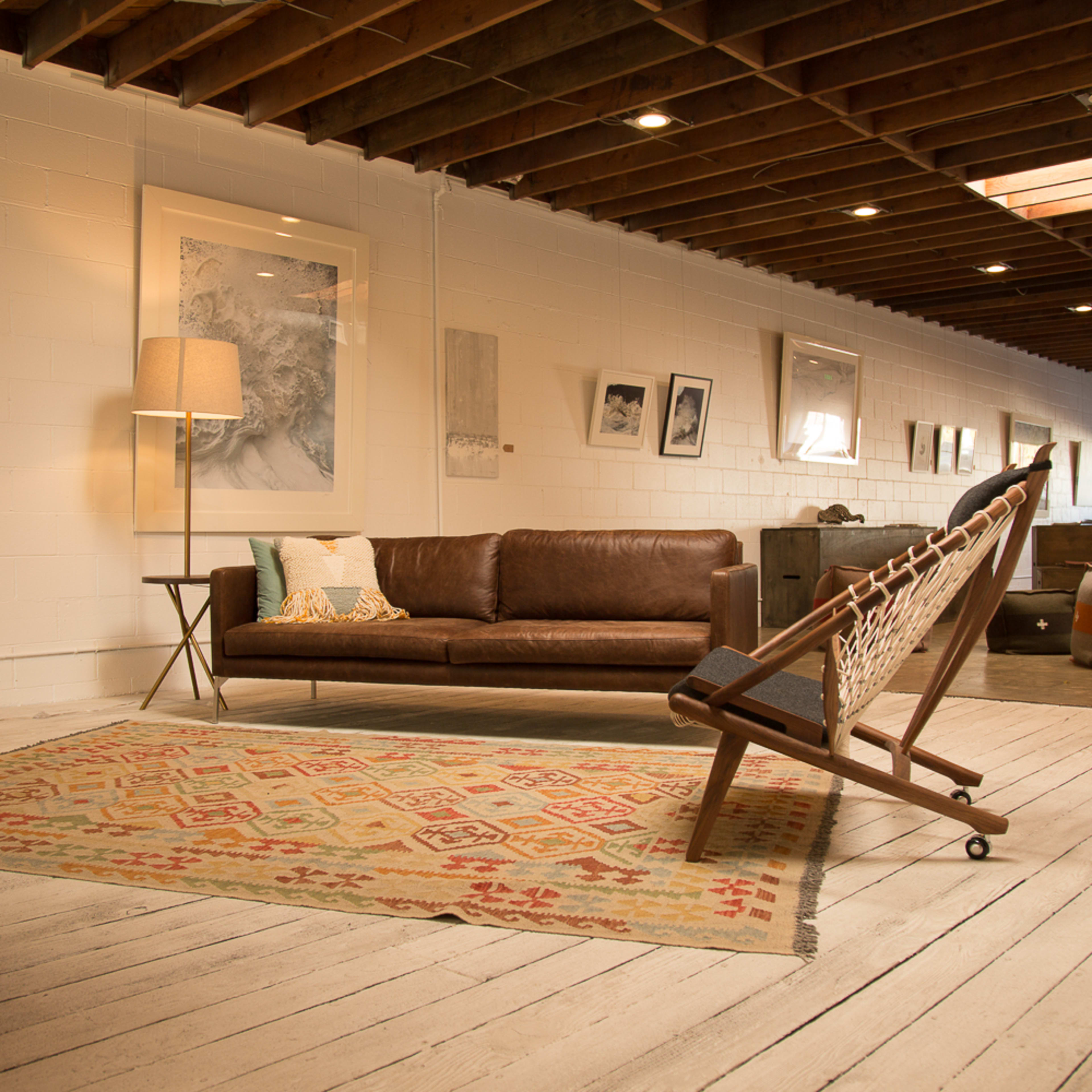 A spacious living area with a leather sofa, a mid-century lamp, and a wooden rocking chair on a patterned rug, surrounded by various framed artworks on the walls.