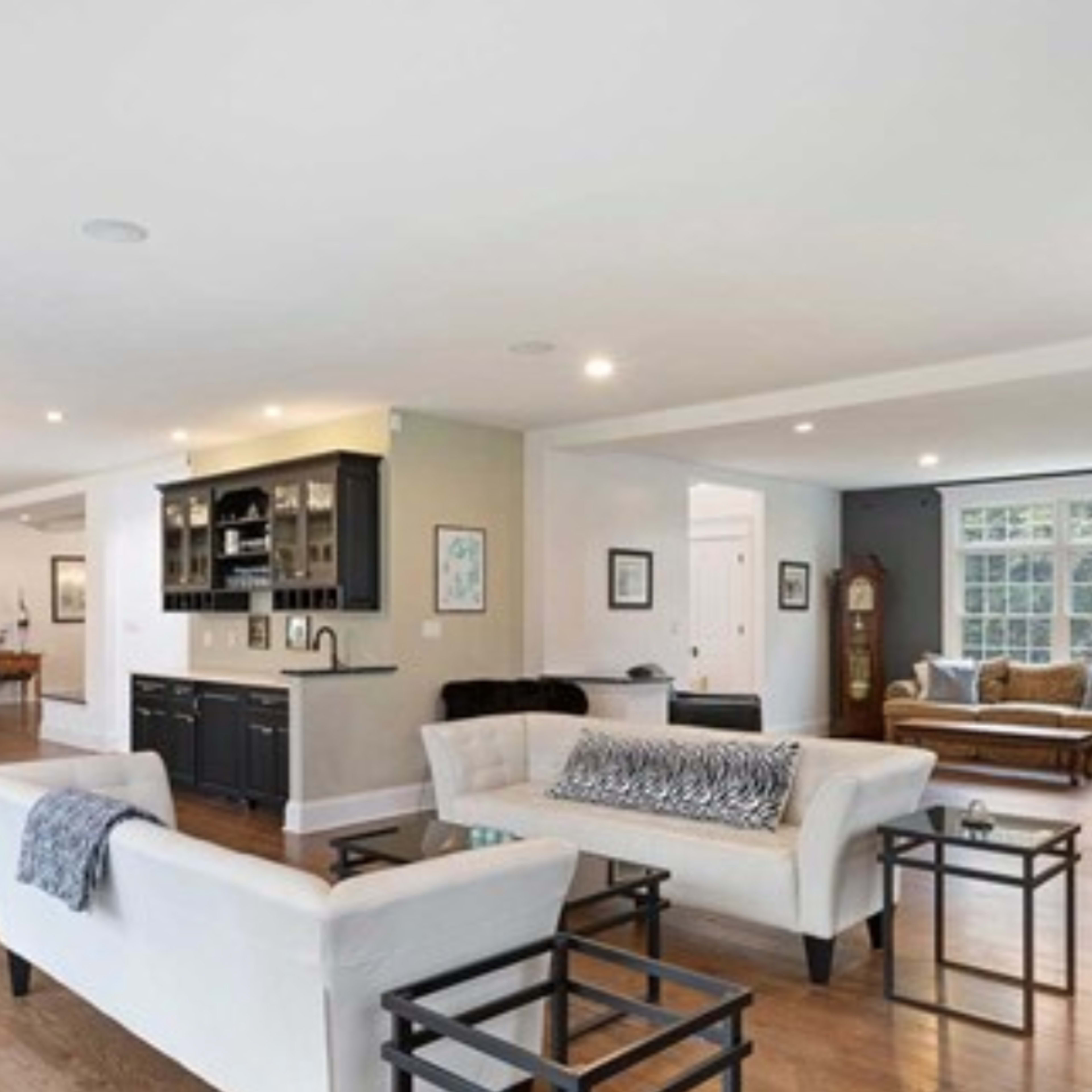 A spacious, modern open-concept living area with a living room, dining area, and kitchen, featuring light-colored furniture and hardwood floors.