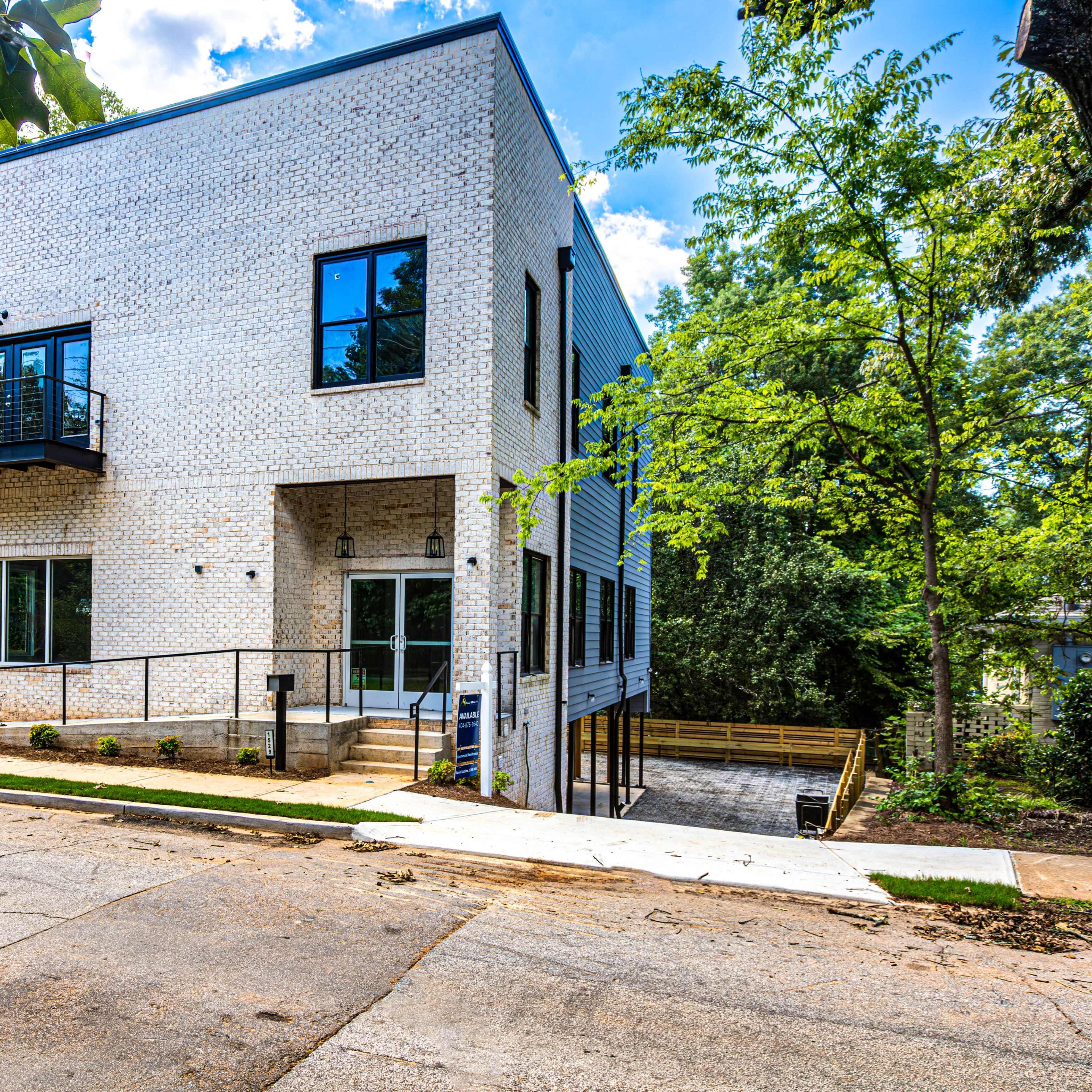 A modern two-story building with white brick exterior and large windows, situated on a sloped street surrounded by greenery.