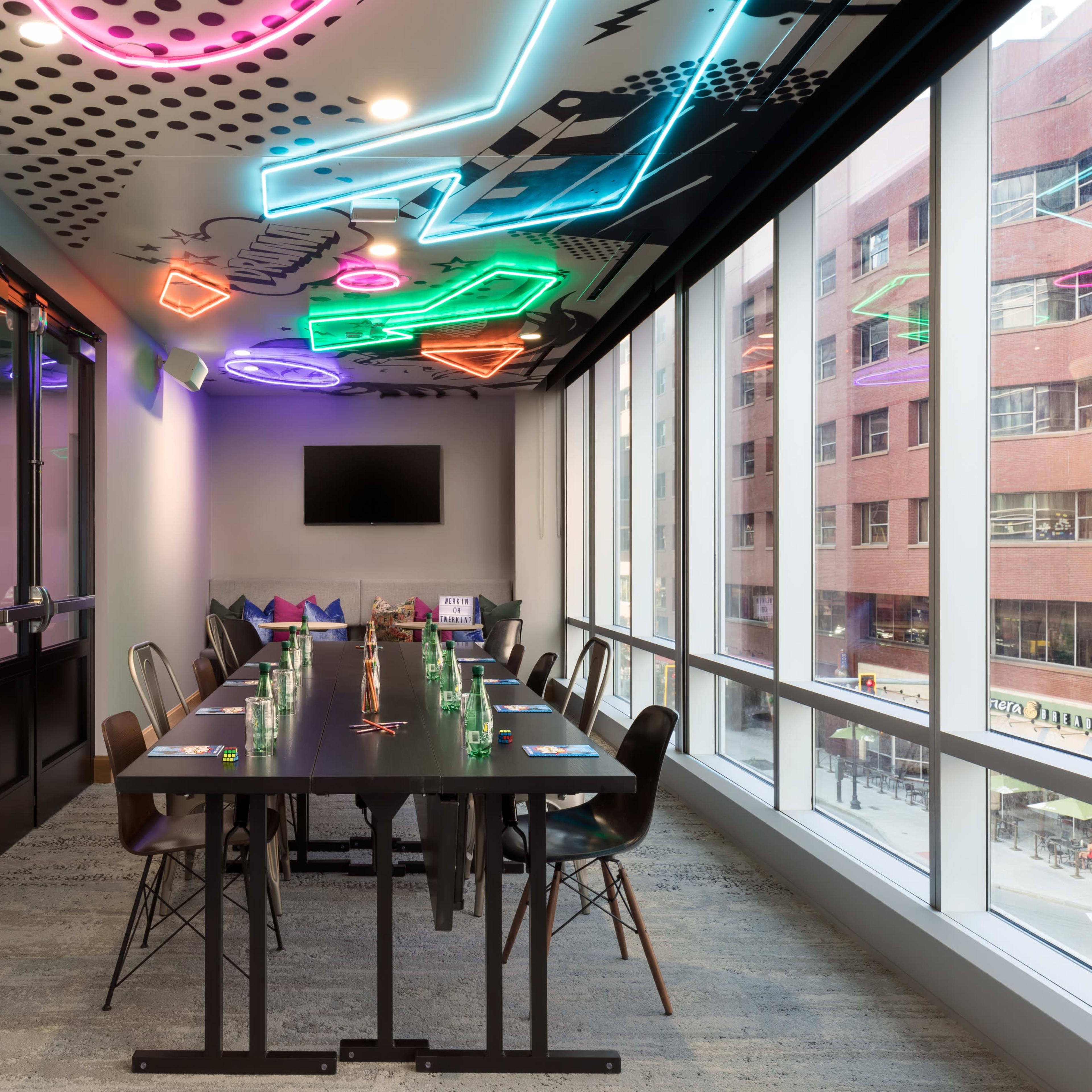 A meeting room features a long black table surrounded by chairs, with colorful neon lights and a wall art piece emphasizing the theme of music.
