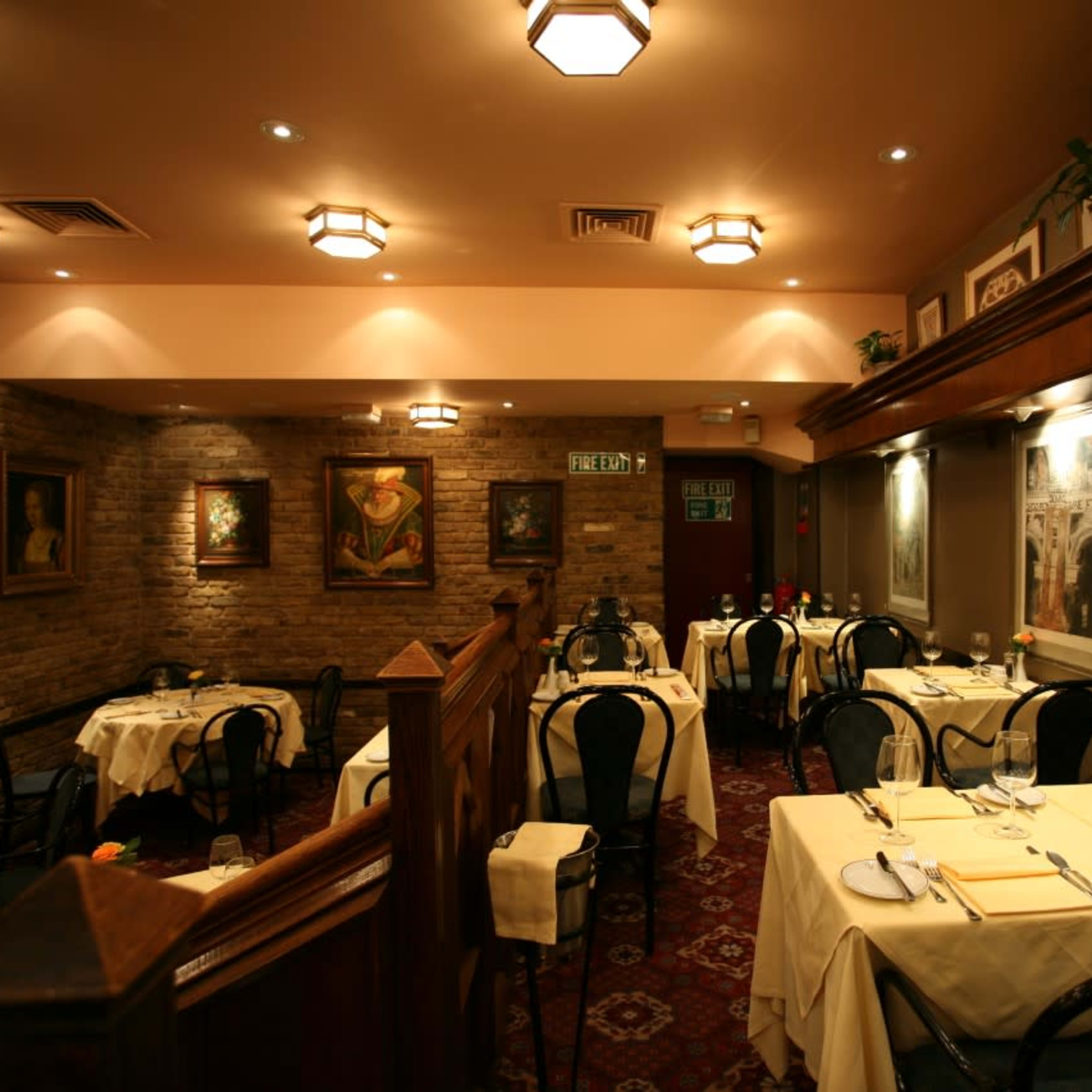 A cozy restaurant interior with tables set for dining, featuring brick walls and decorative art pieces.