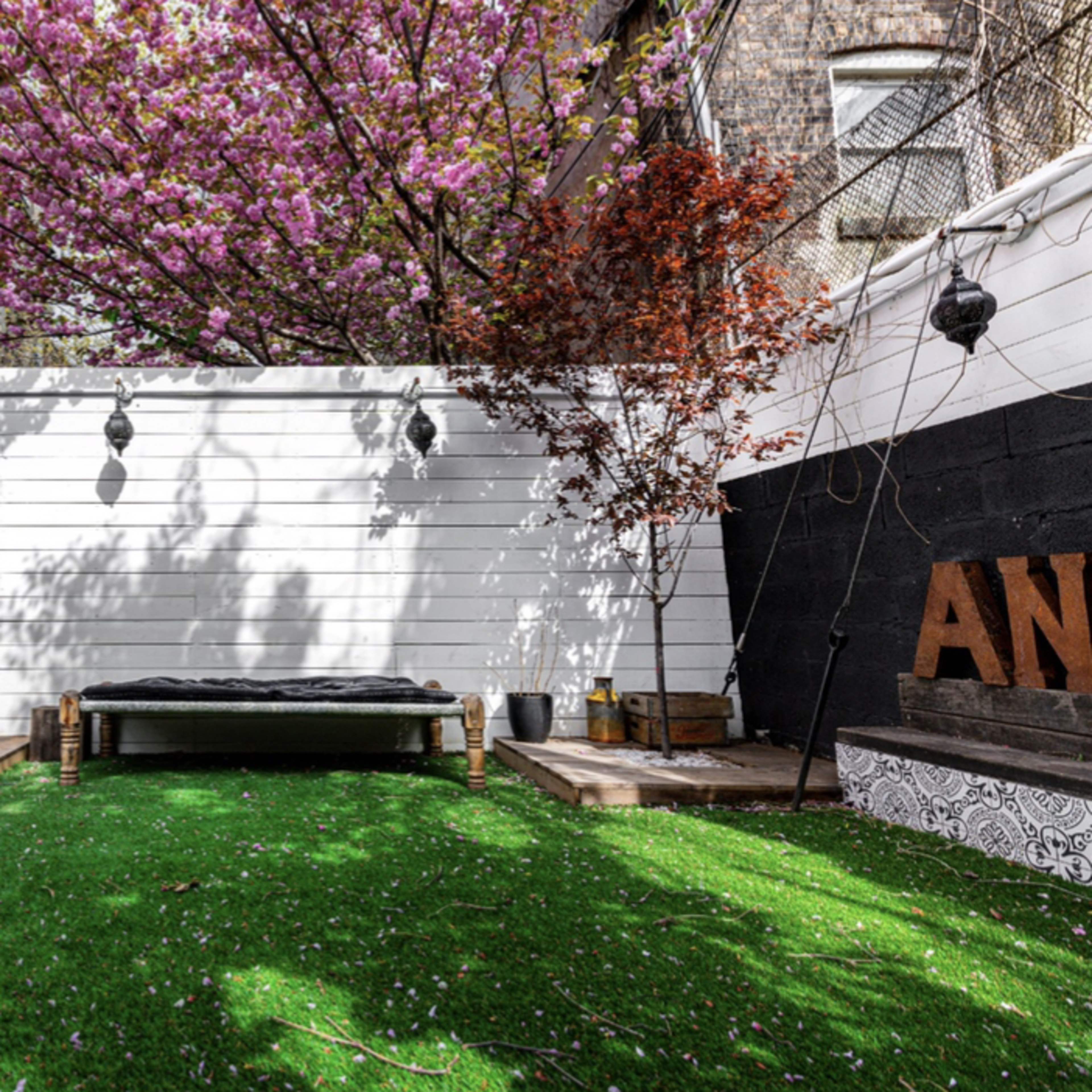 A backyard with artificial grass, a wooden deck, a lounging area, and a blooming tree providing shade.
