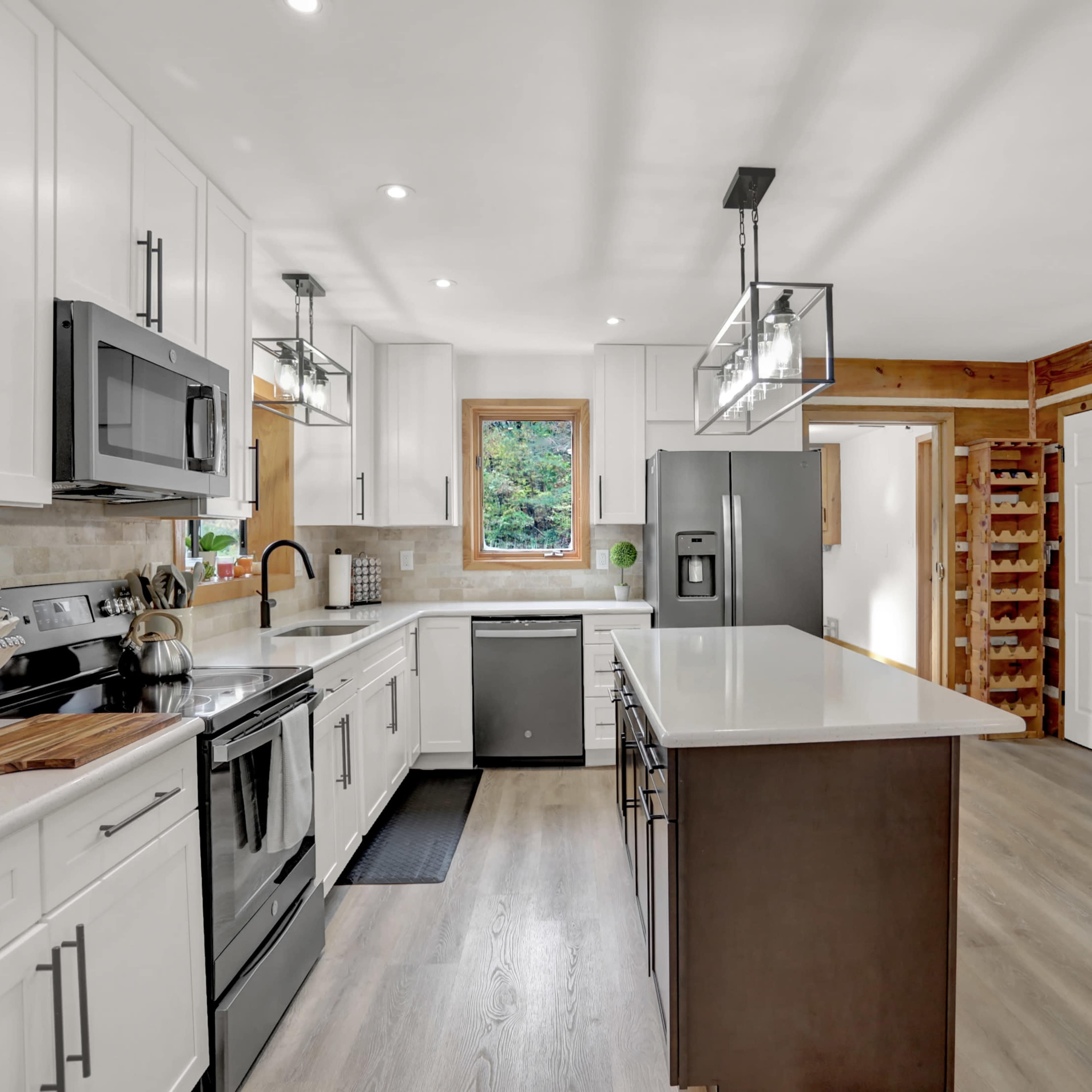 A modern kitchen featuring white cabinetry, stainless steel appliances, a large island with a dark countertop, and wooden accents on the walls.