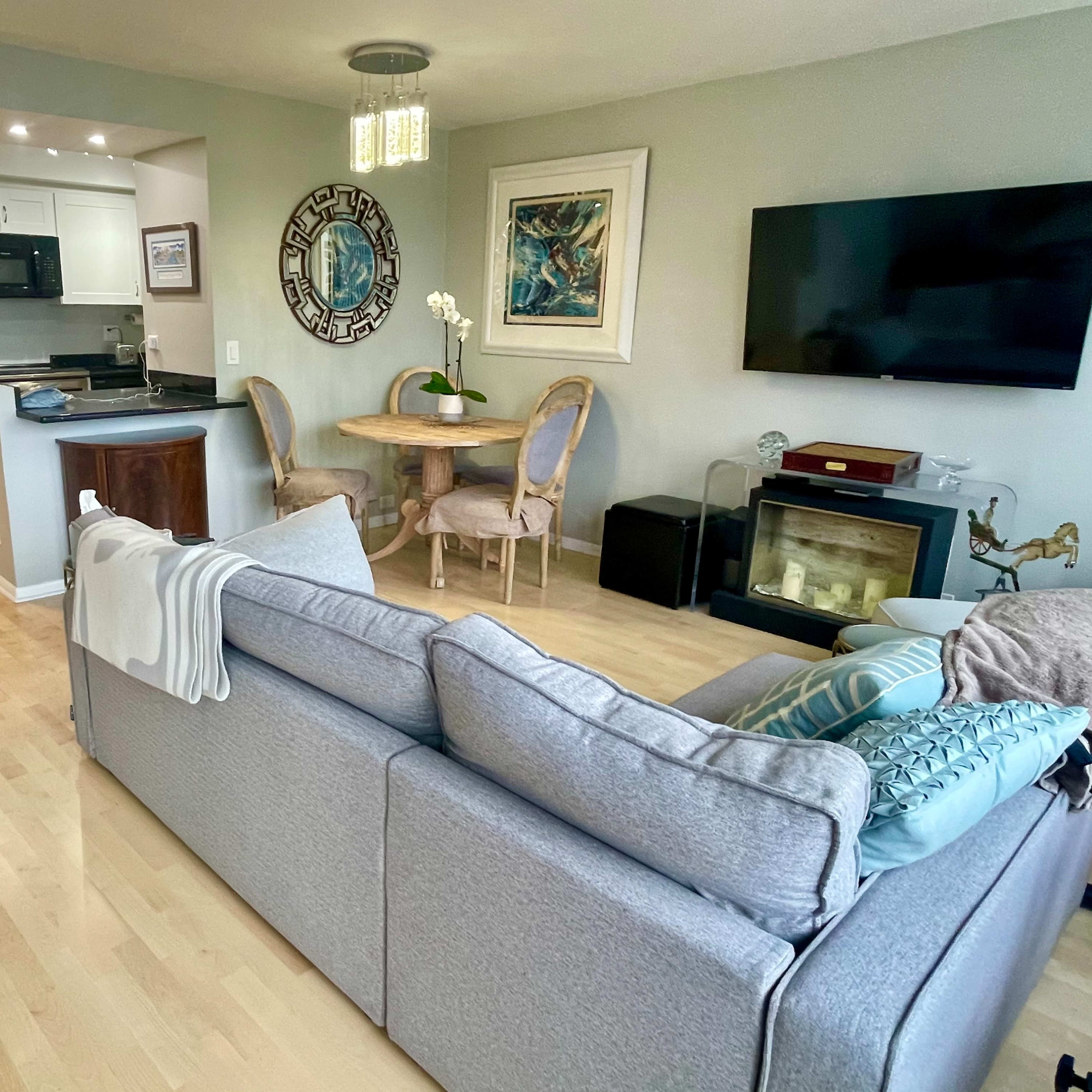 A modern, open-concept living space featuring a gray sofa, a round dining table with chairs, and a kitchenette with black appliances.