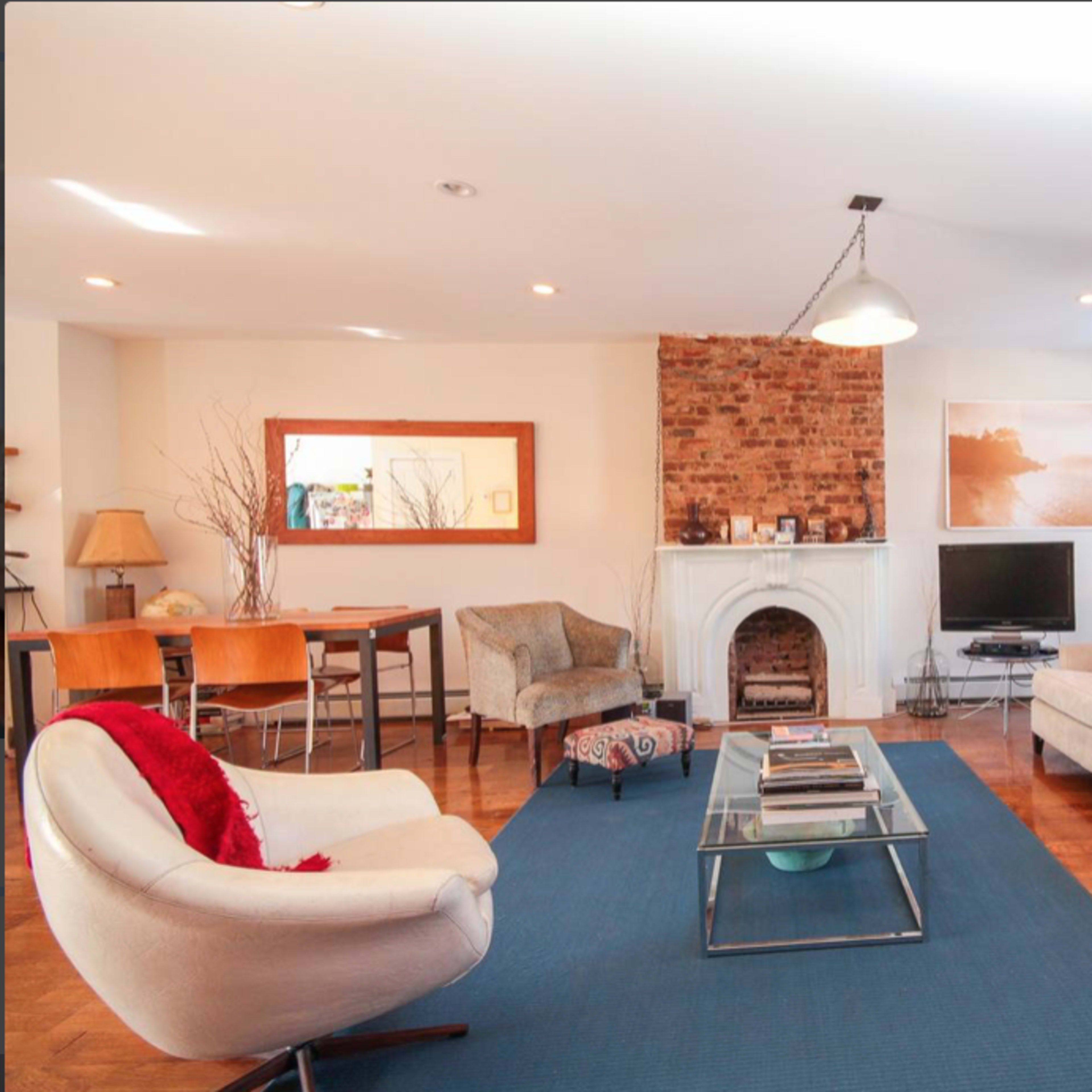 A cozy living room features a brick fireplace, two sofas, and a coffee table, with a guitar resting against one wall.