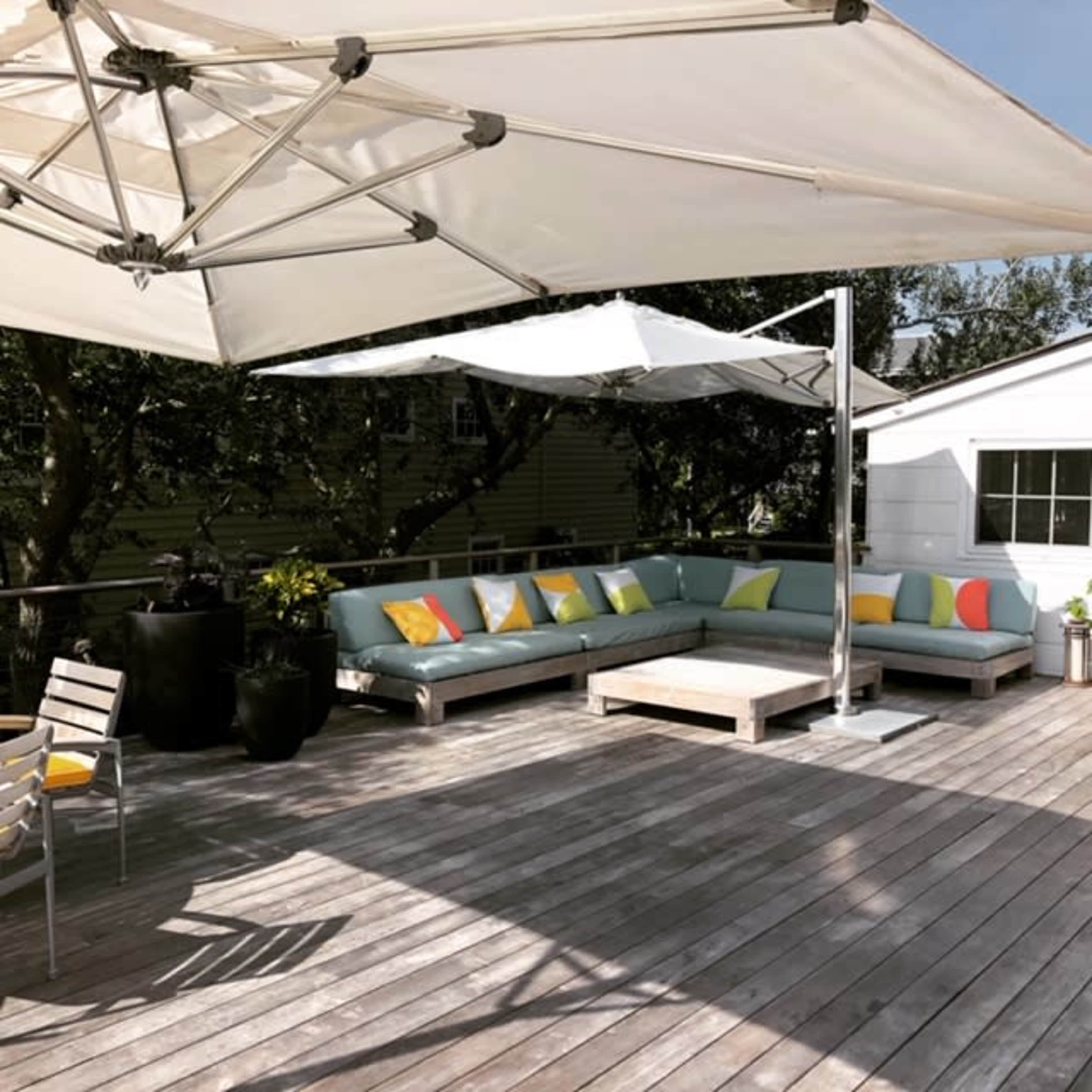 A covered outdoor seating area features a sectional sofa with colorful cushions and a coffee table on a wooden deck.