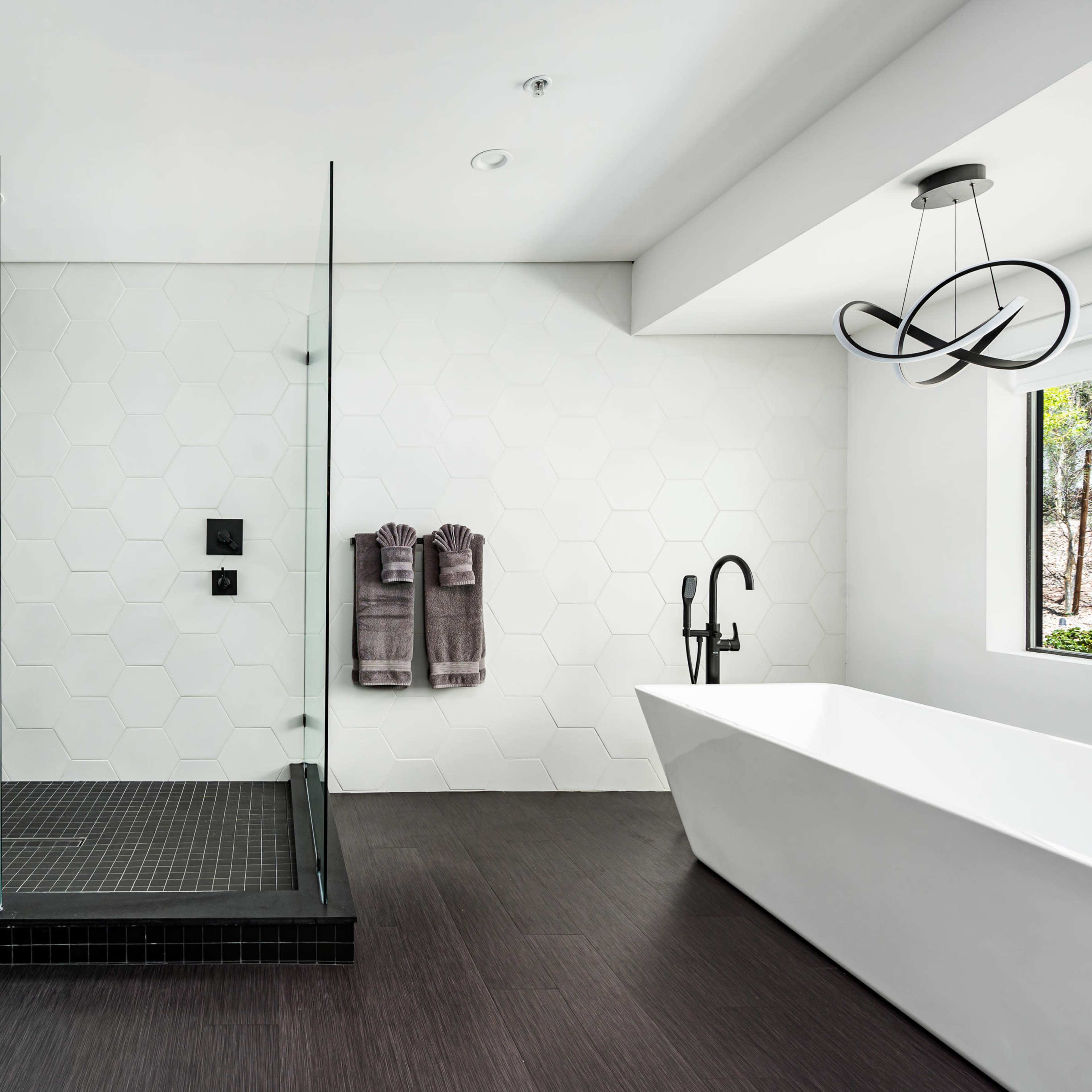 A modern bathroom featuring a walk-in glass shower, a freestanding bathtub, and hexagonal wall tiles.