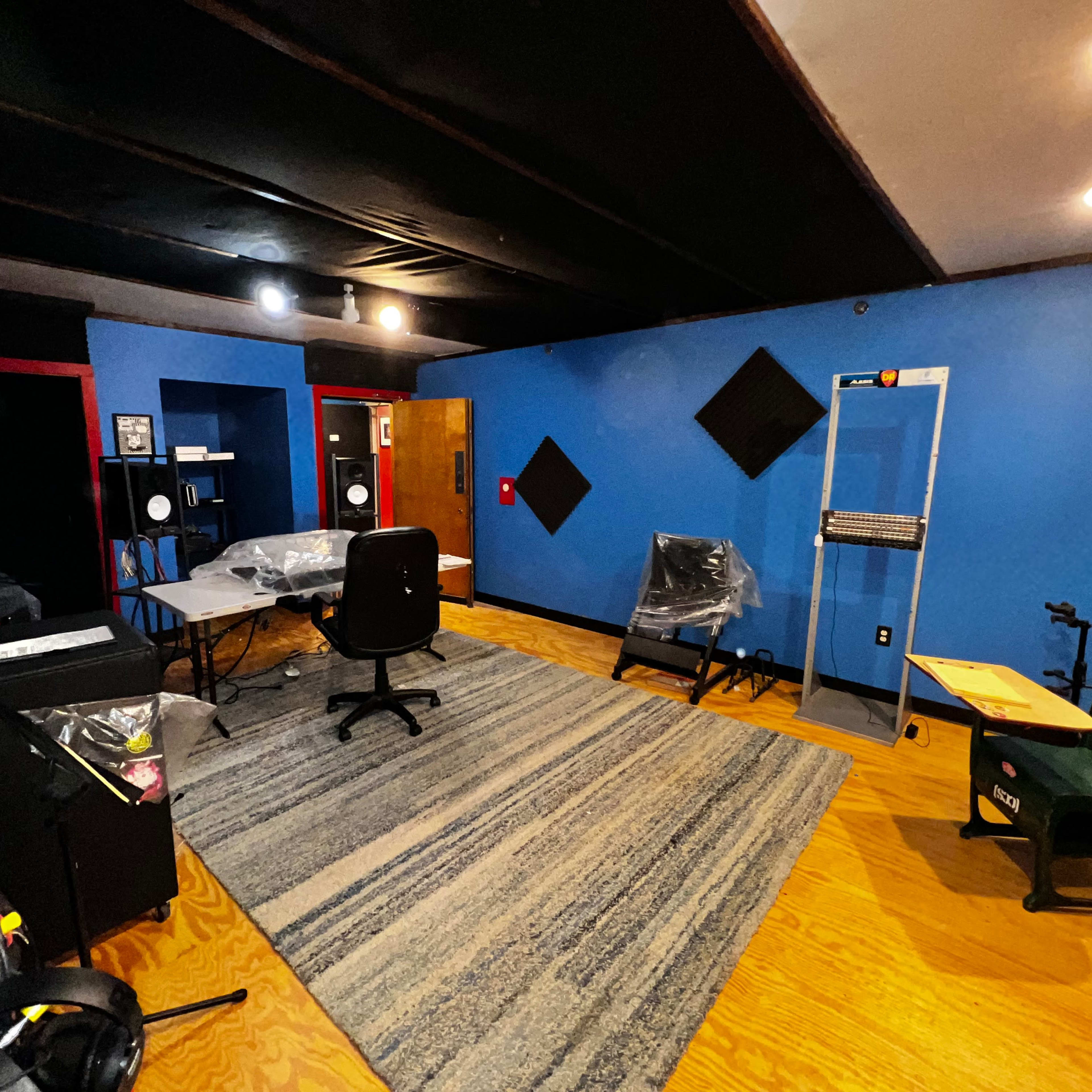 A spacious room with blue walls, wooden flooring, and various pieces of furniture including a desk, chairs, and soundproofing panels.