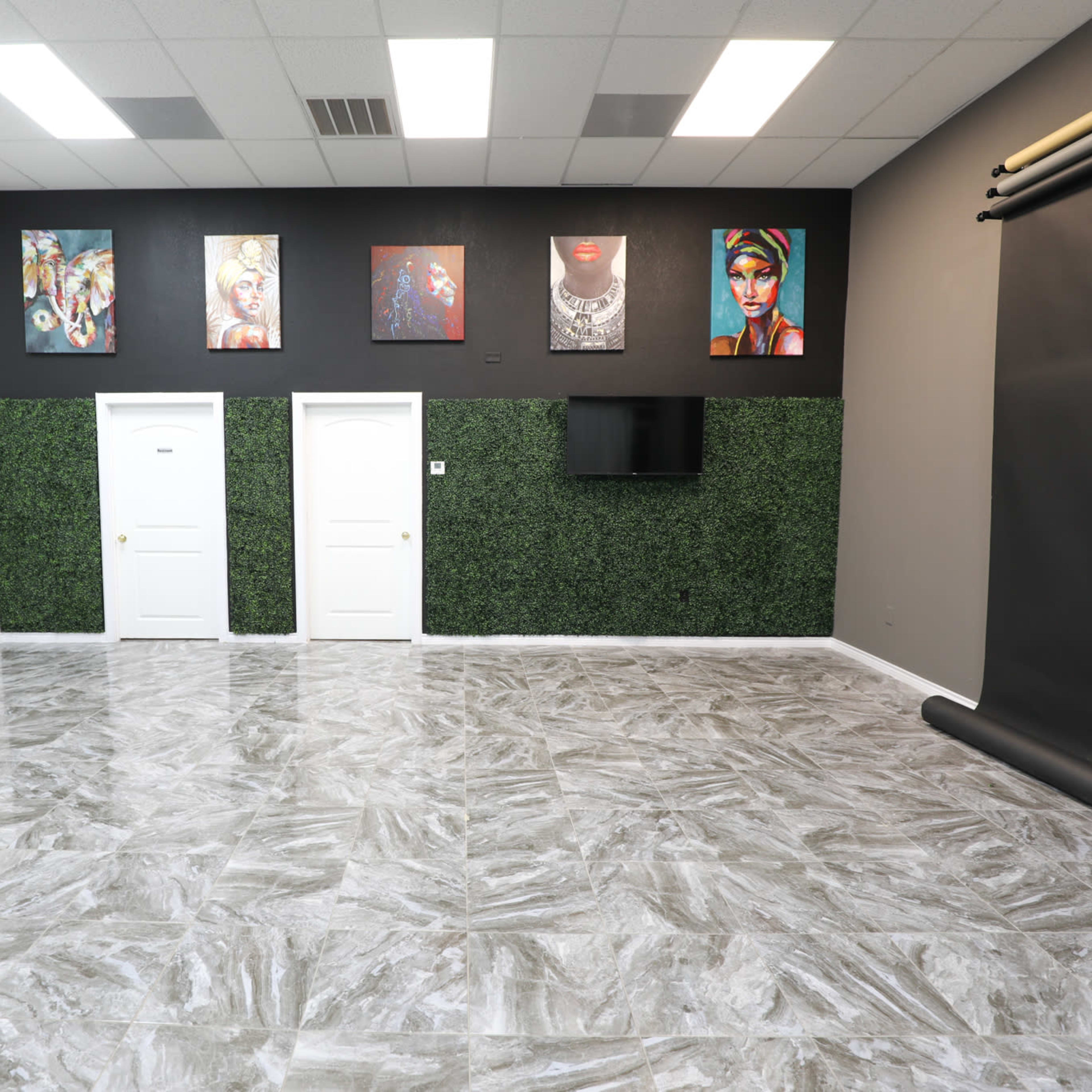 A spacious room with a polished floor, two doors on a green accent wall, framed artwork, and a black photographic backdrop.